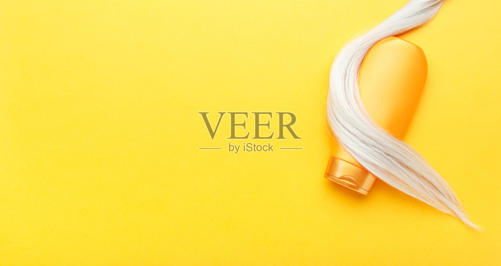 金色的洗发水瓶子包裹在一缕金色的头发上，橙色的背景。染过发丝的桔色瓶洗发精。护发化妆品沐浴美容产品护发。俯视图拷贝空间照片摄影图片