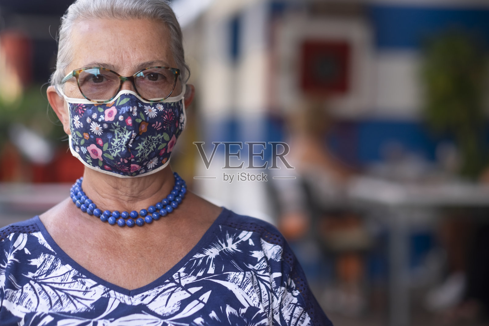 一位因冠状病毒而戴着花面具的老年妇女的肖像——退休期间活跃老年人的概念照片摄影图片