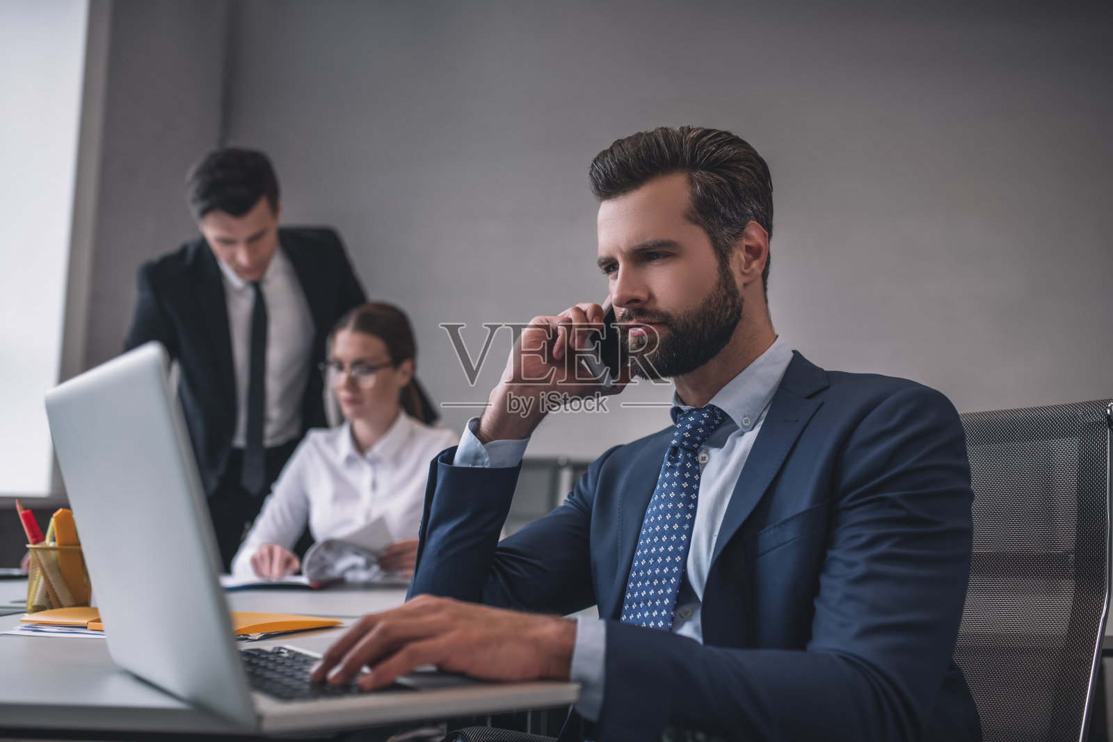 在笔记本电脑前拿着智能手机的男人，同事在附近照片摄影图片