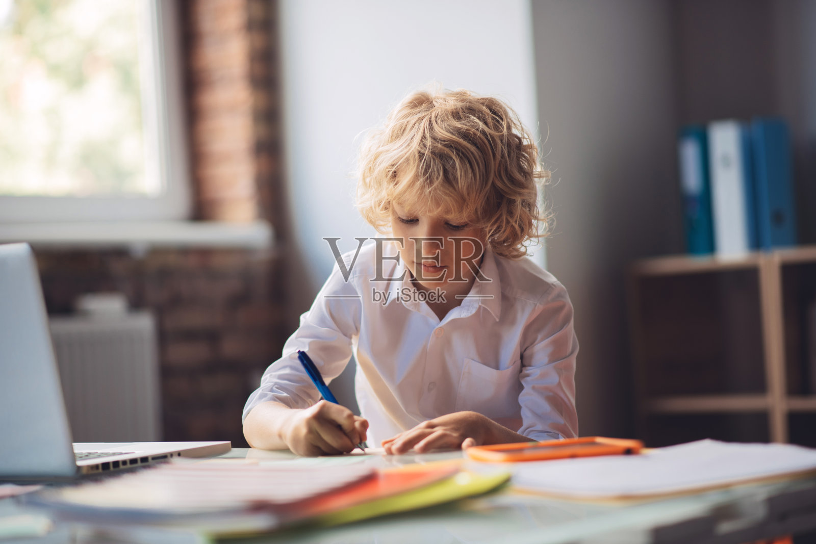 可爱的金发男孩坐在桌旁写东西照片摄影图片