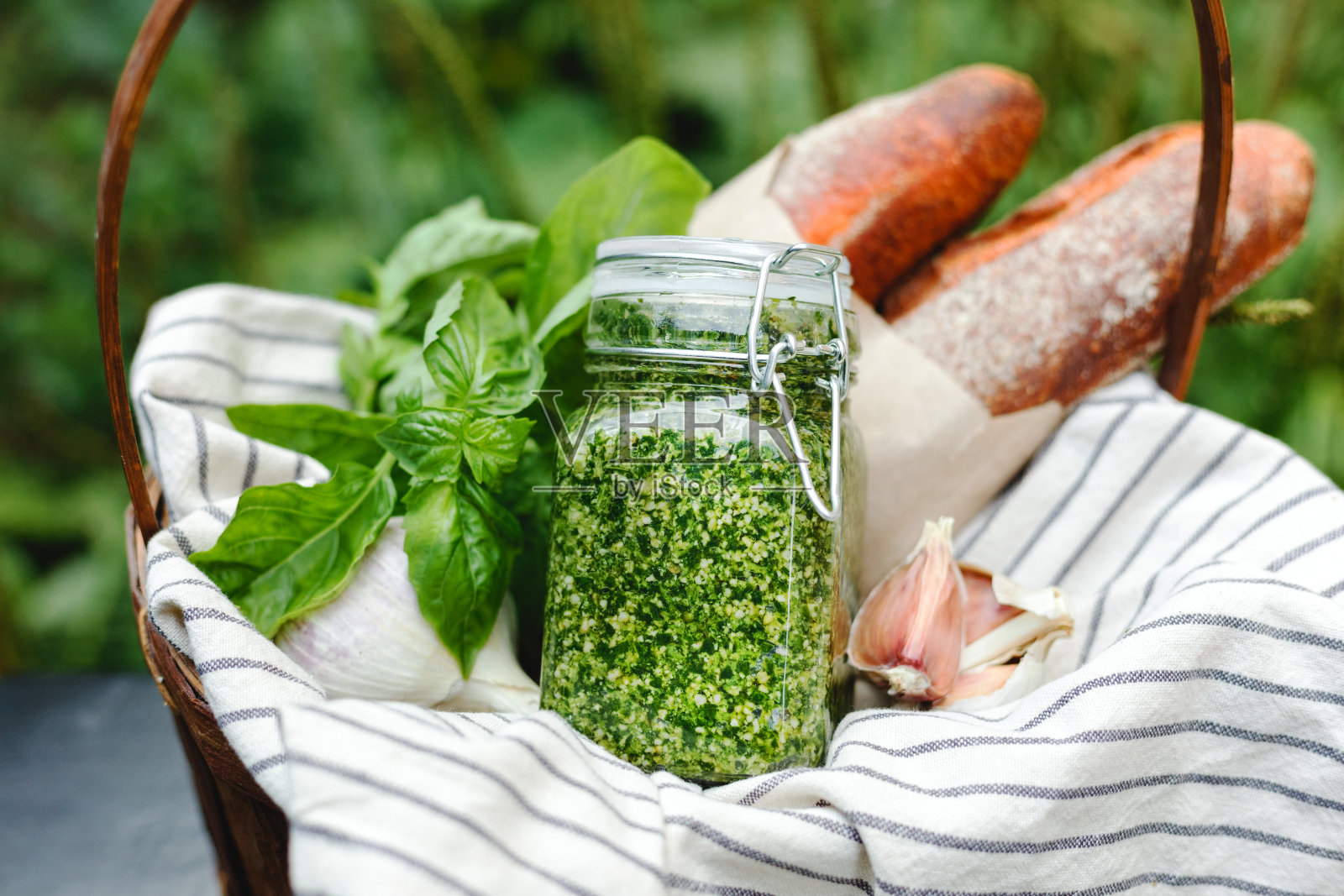 野餐篮子，准备新鲜的大蒜面包或意式烤面包，传统意大利酱法棍开胃菜-自制的香蒜酱在玻璃罐中，配料有罗勒，松子和面包户外。照片摄影图片