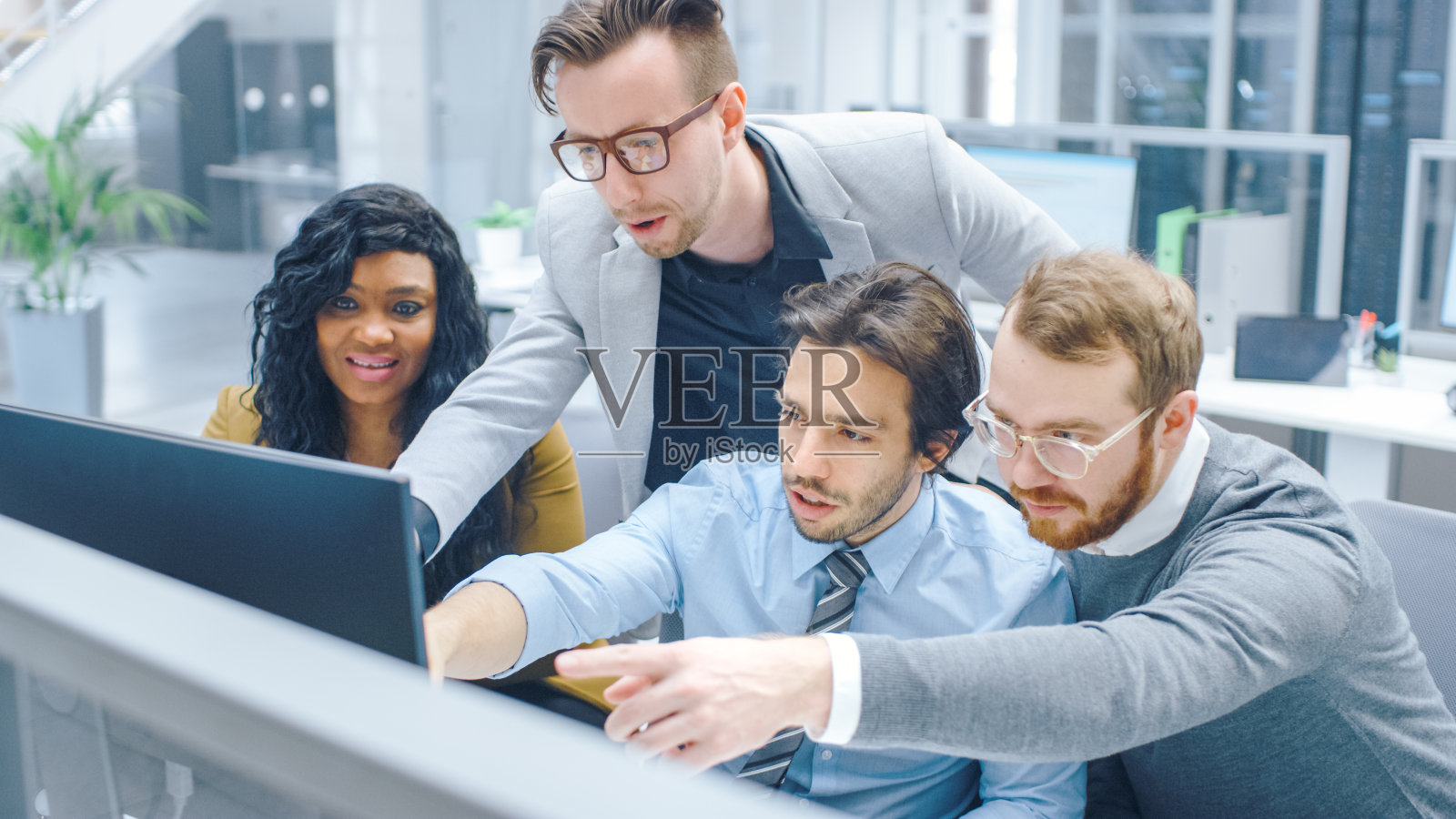 在现代办公室:多样化的团队的商人和女商人在电脑上工作，进行讨论，试图找到问题的解决方案。年轻的商业人士在屏幕上交谈和指向照片摄影图片