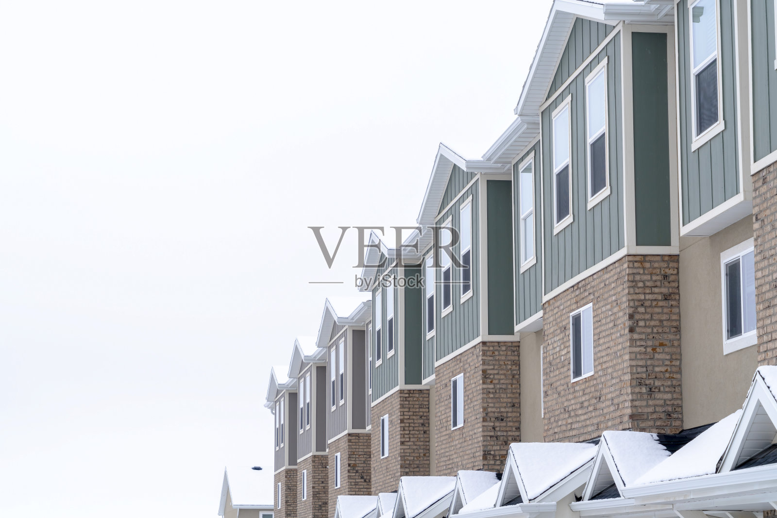 带有砖墙、垂直壁板和雪屋顶的联排住宅的上层照片摄影图片