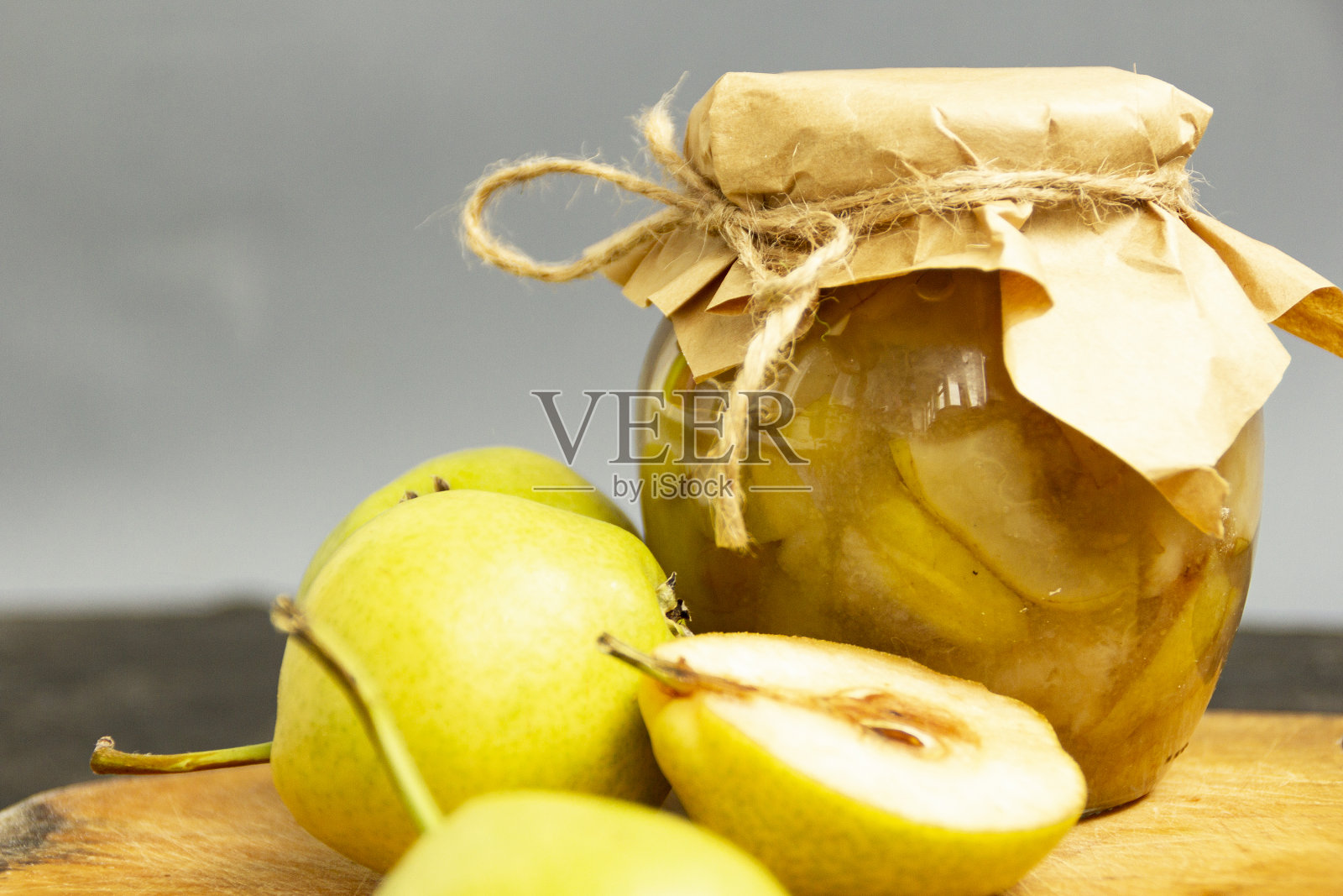 玻璃罐里的梨酱。罐子用牛皮纸包着，用黄麻绳绑着。切菜板上放着甜果酱，旁边放着新鲜的黄梨照片摄影图片
