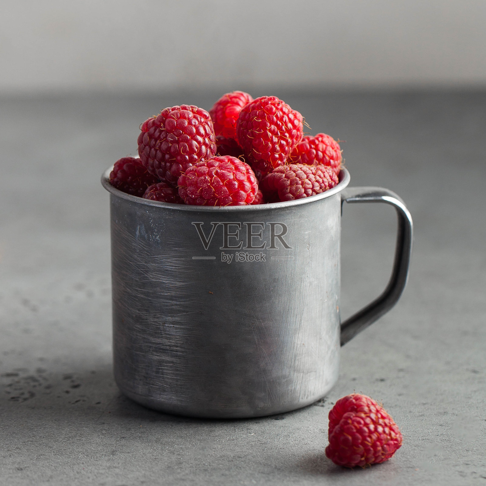 新鲜成熟的覆盆子放在一个木碗里，背景是灰色的。健康饮食的概念。副本的空间。照片摄影图片