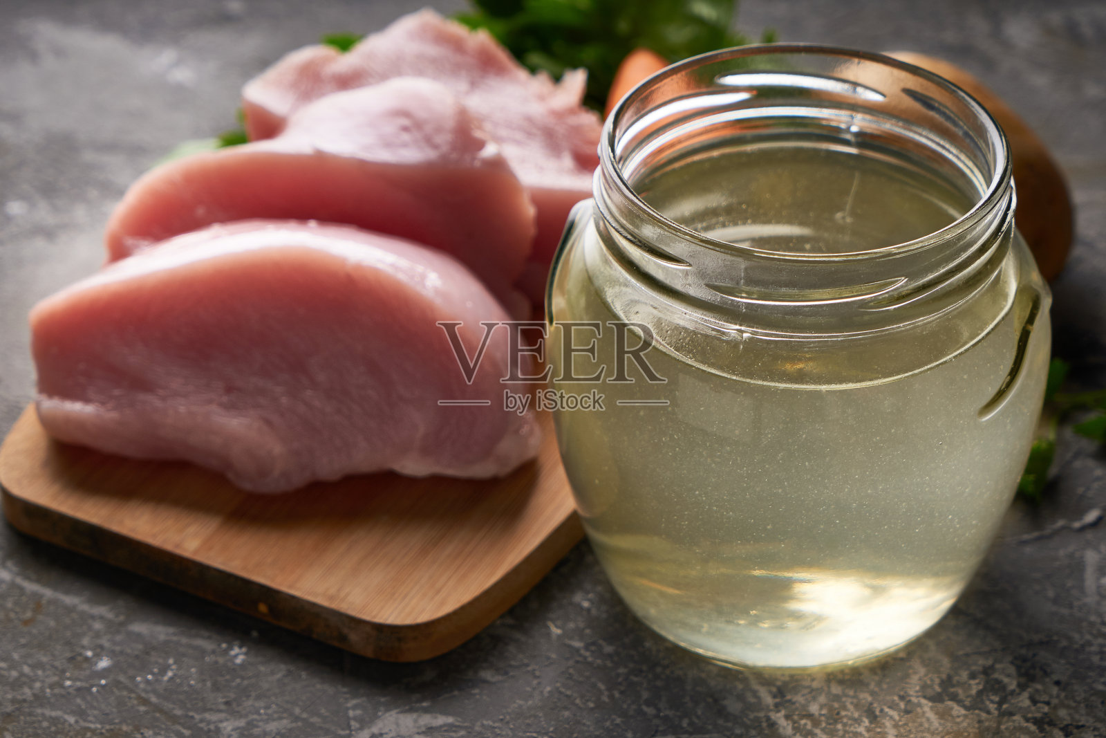 新鲜的家禽肉汤在一个玻璃罐里，在桌子上的蔬菜和新鲜的禽肉块照片摄影图片