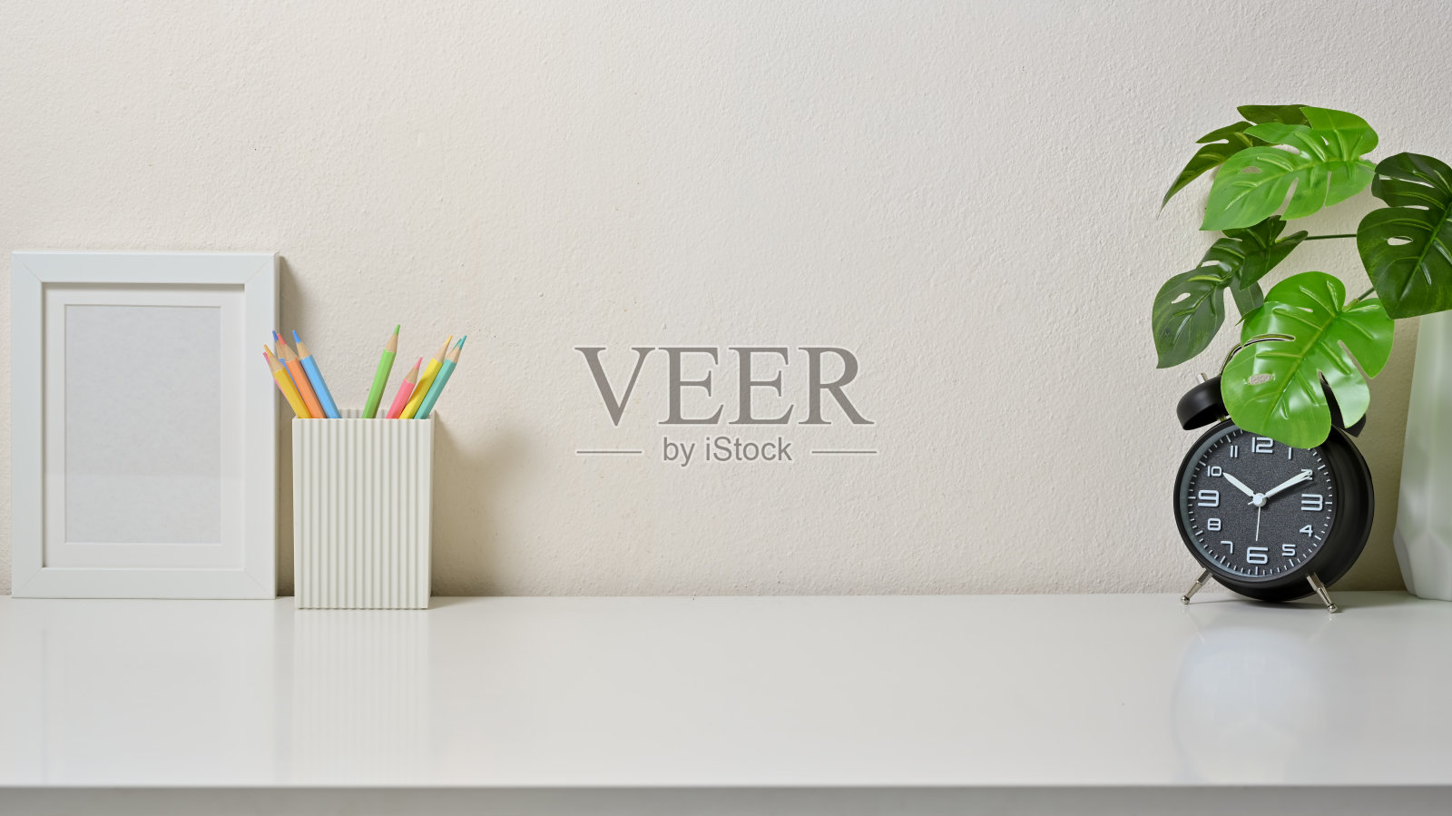 现代办公空间，白色桌子上有相框，彩色铅笔，时钟和花瓶。前视图。照片摄影图片