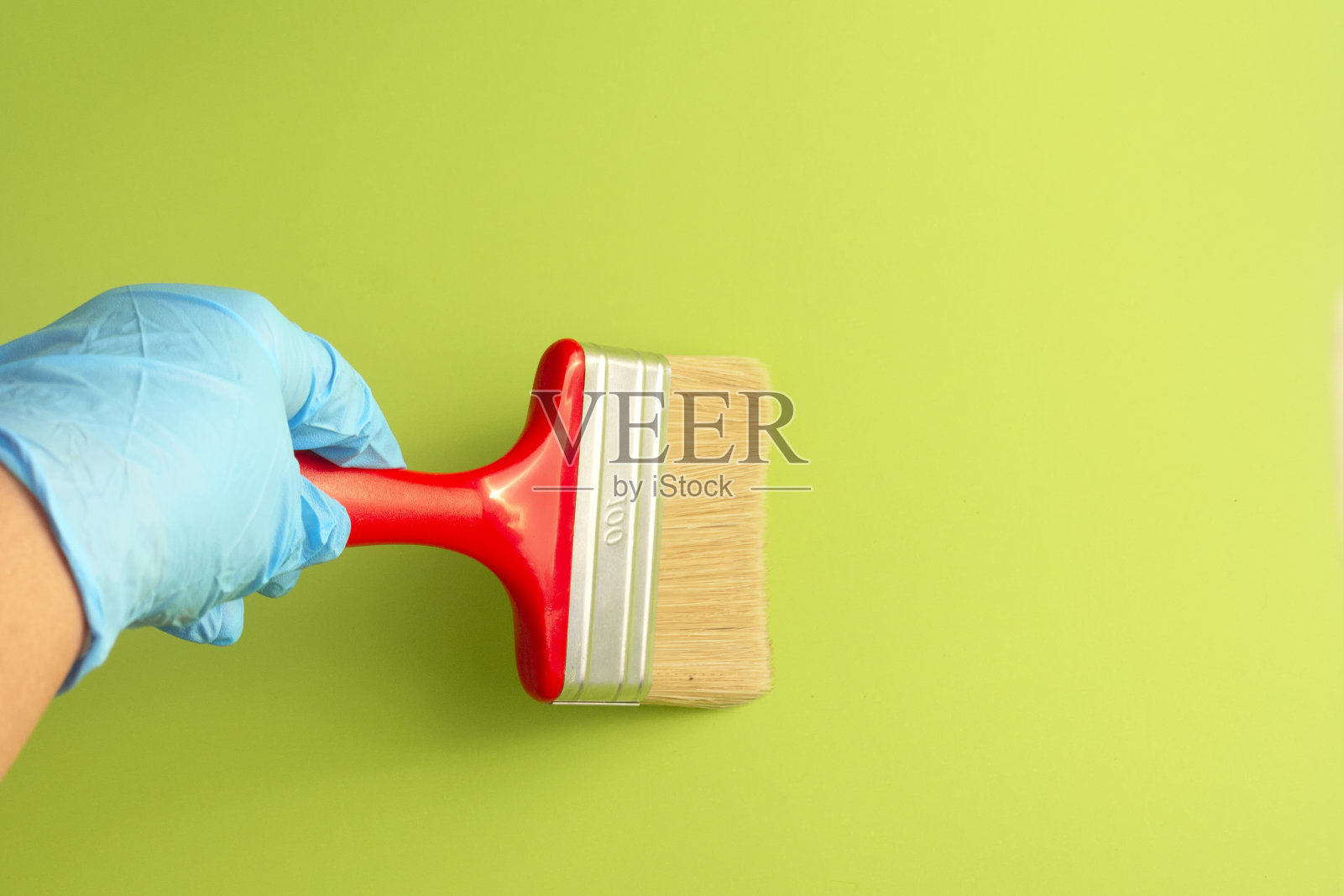 戴着蓝色手套的女性手拿着红色的画笔在绿色的背景上作画。修复的概念。照片摄影图片