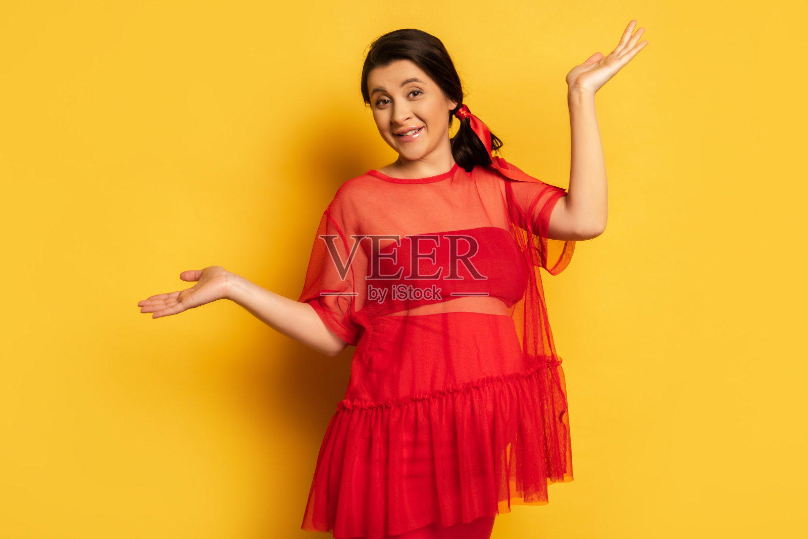 身穿红色外衣的孕妇站在黄色衣服上张开双臂看着镜头照片摄影图片