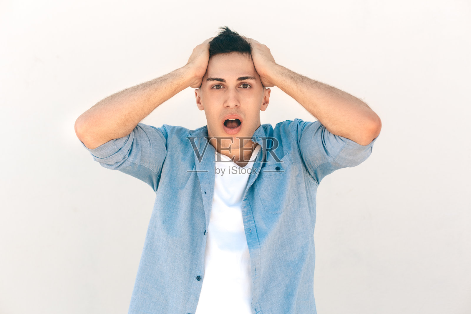 户外休闲。型男孤立地站在白色的捧着头，嘴张得很震惊照片摄影图片