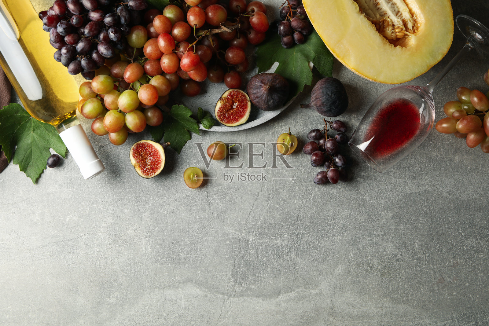以葡萄、葡萄酒、无花果和甜瓜为灰色背景照片摄影图片