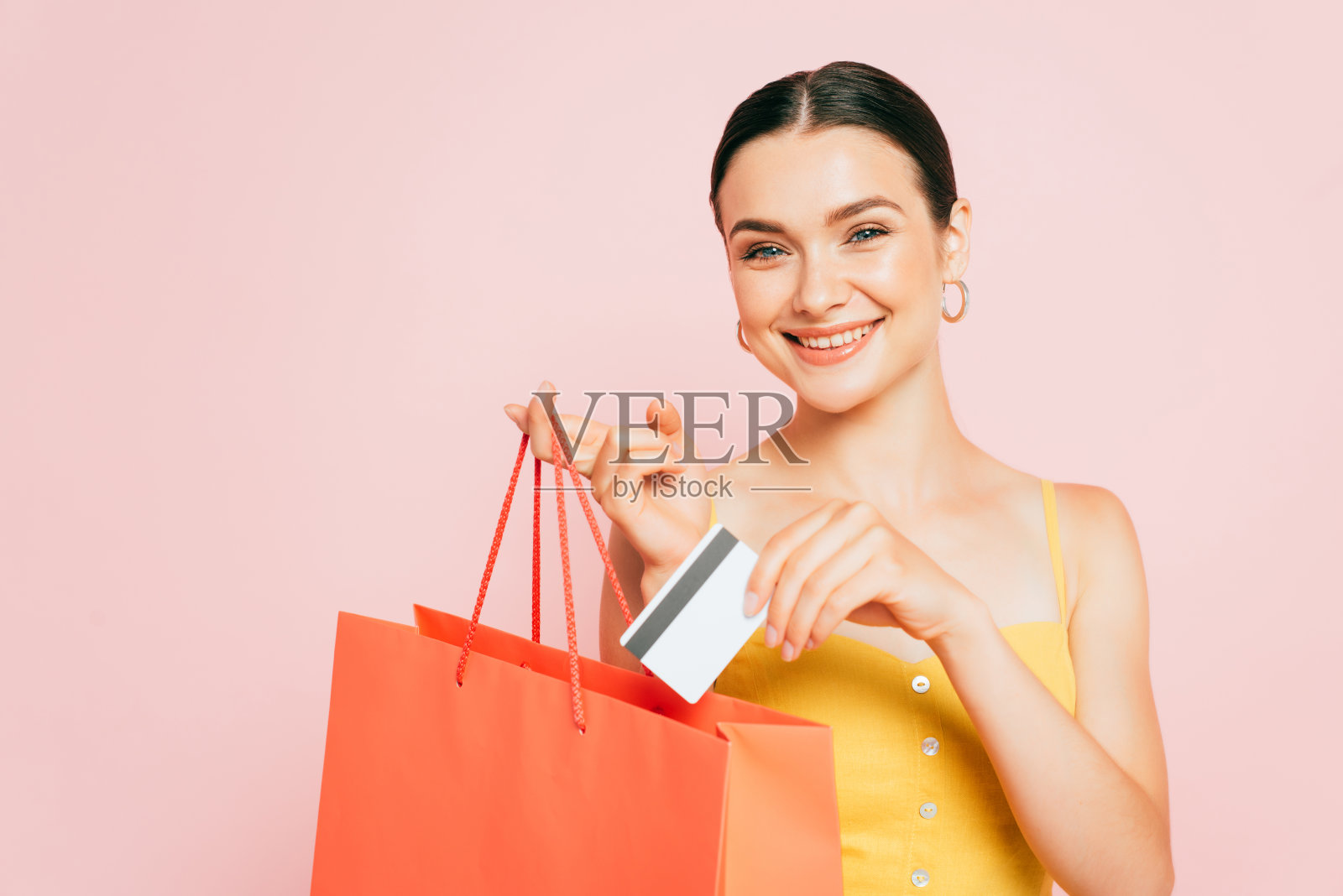 黑发姑娘把信用卡放在购物袋里，粉色隔离照片摄影图片