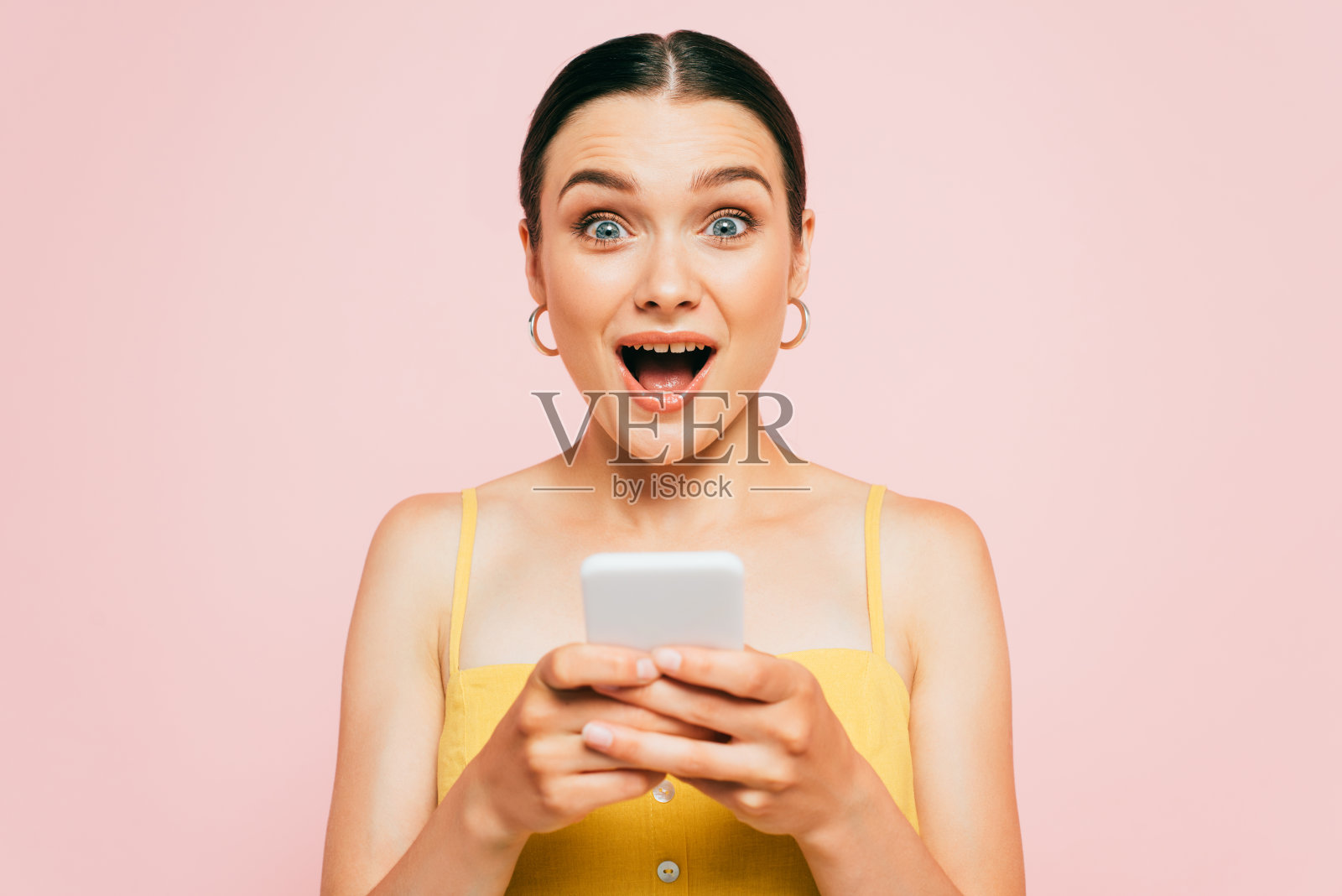 震惊的黑发年轻女子使用智能手机隔离粉红色照片摄影图片