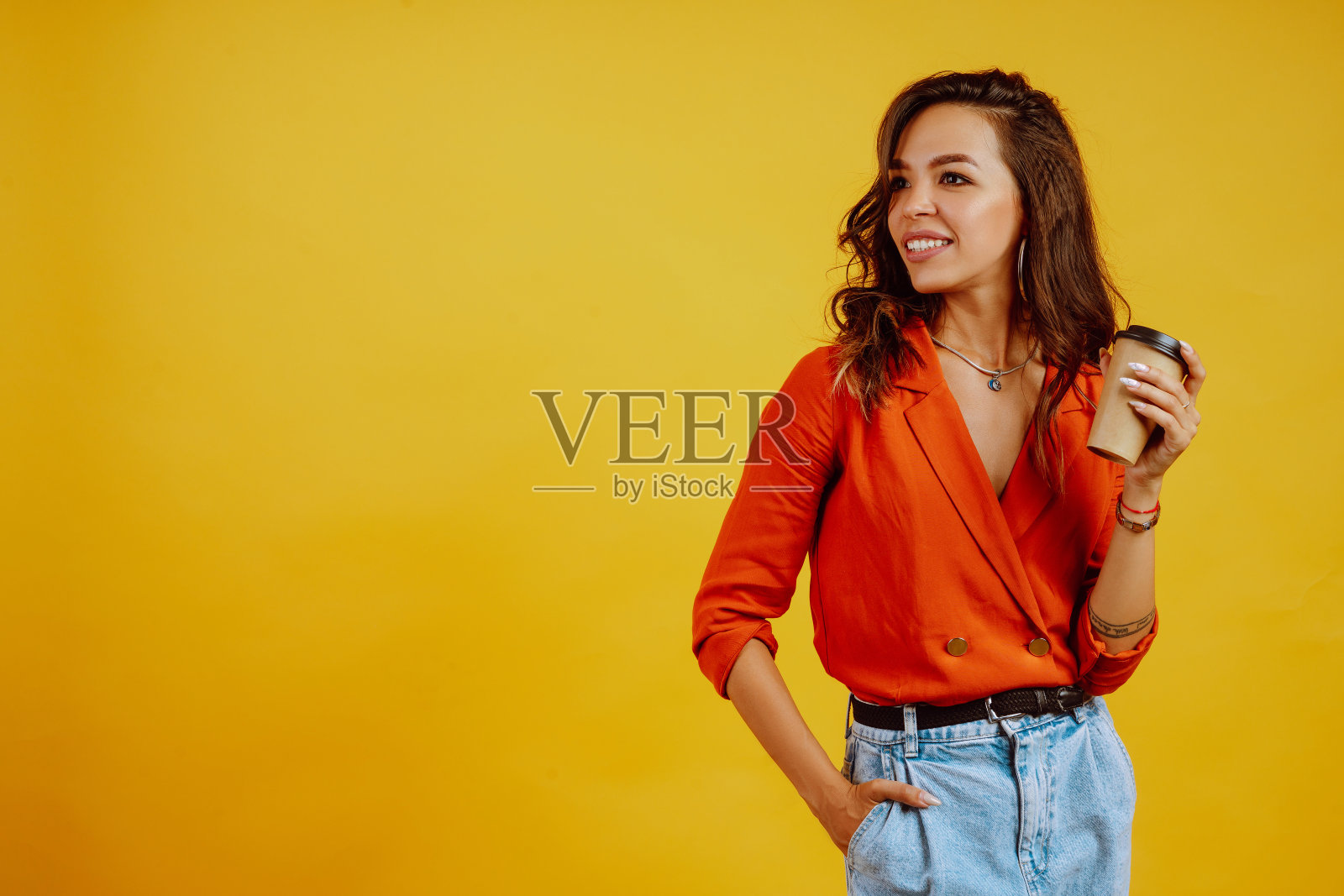 在黄色背景上摆着咖啡姿势的年轻女子。照片摄影图片