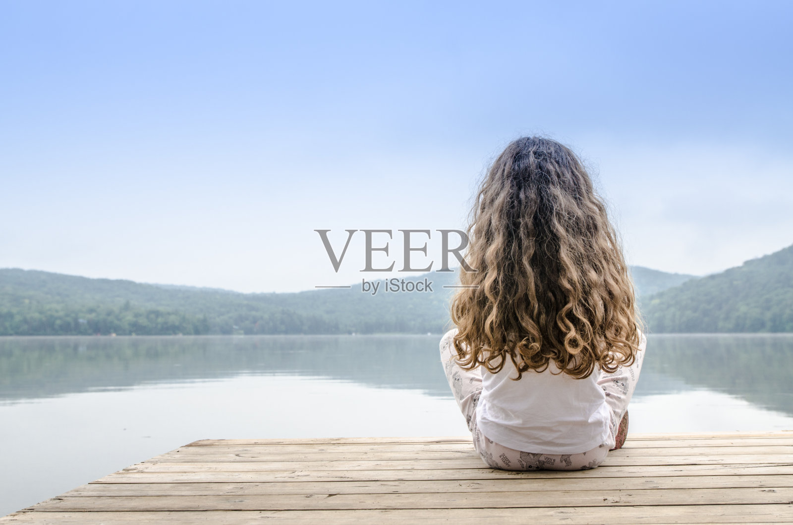 小女孩坐在湖的甲板上照片摄影图片