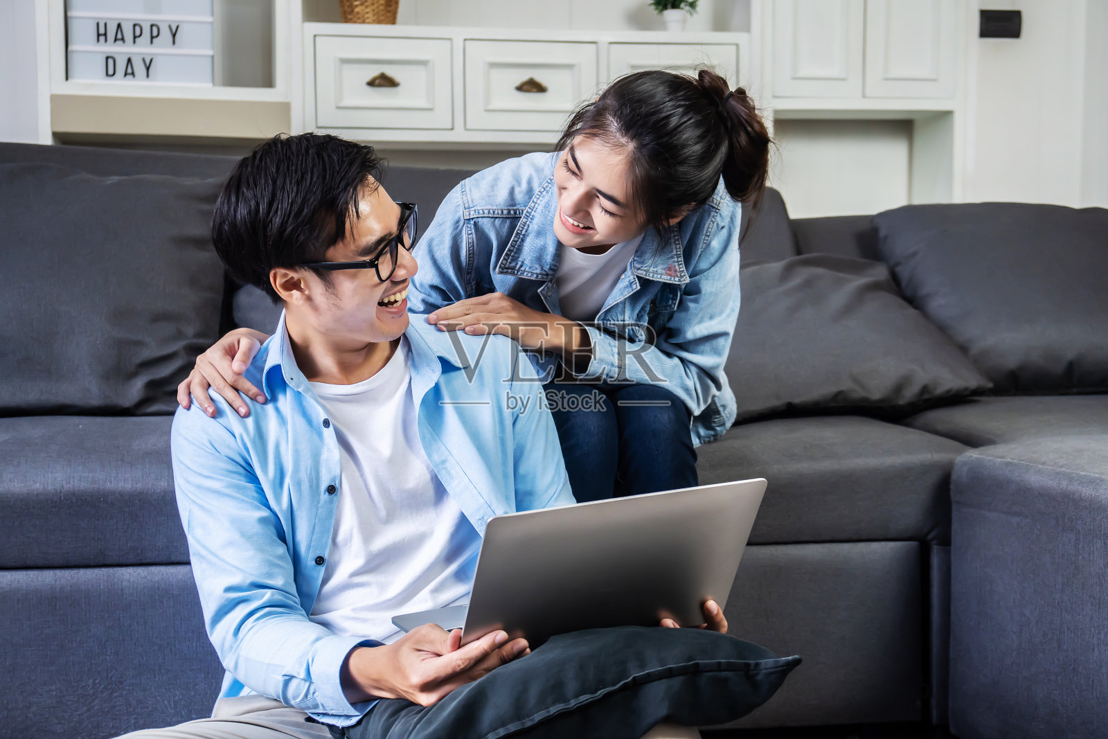 亚洲夫妇微笑，看着对方愉快地聊天。他们坐在家里舒适的沙发上，放松和轻松地购买商品吗照片摄影图片