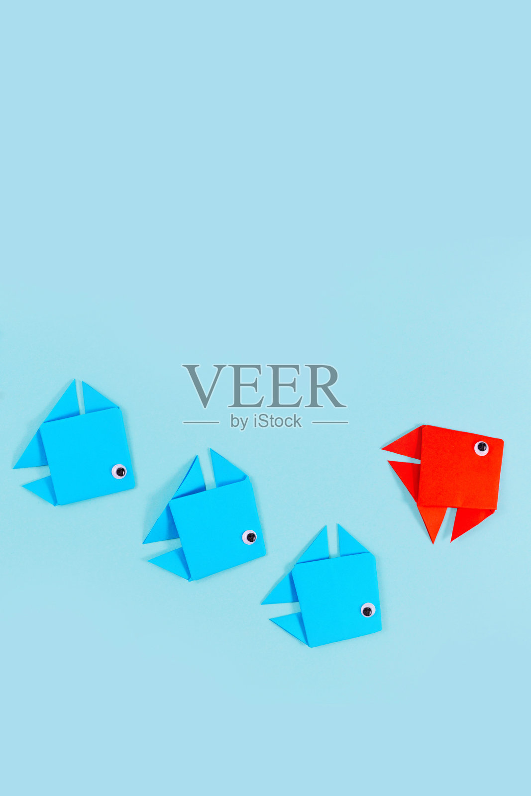 一条红色的折纸鱼在游在蓝鱼的前面时改变方向。照片摄影图片