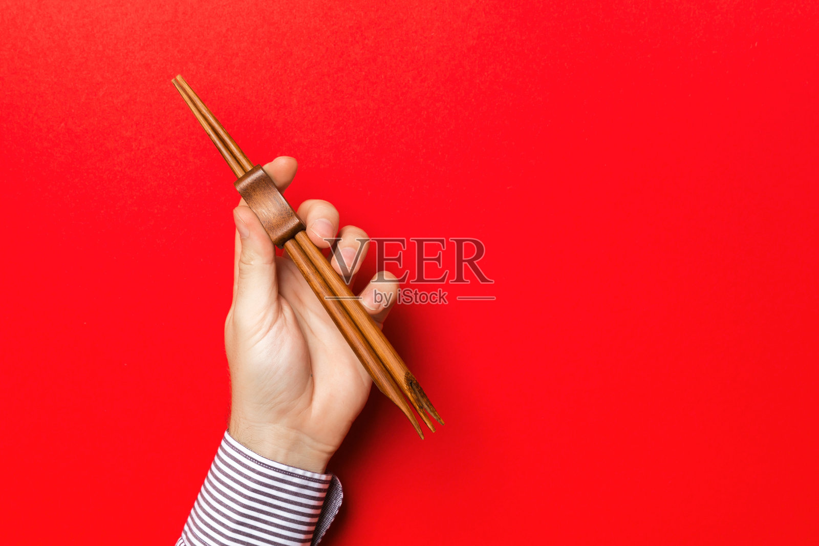红色背景上男性手持筷子的裁剪图像。亚洲美食概念与复制空间照片摄影图片