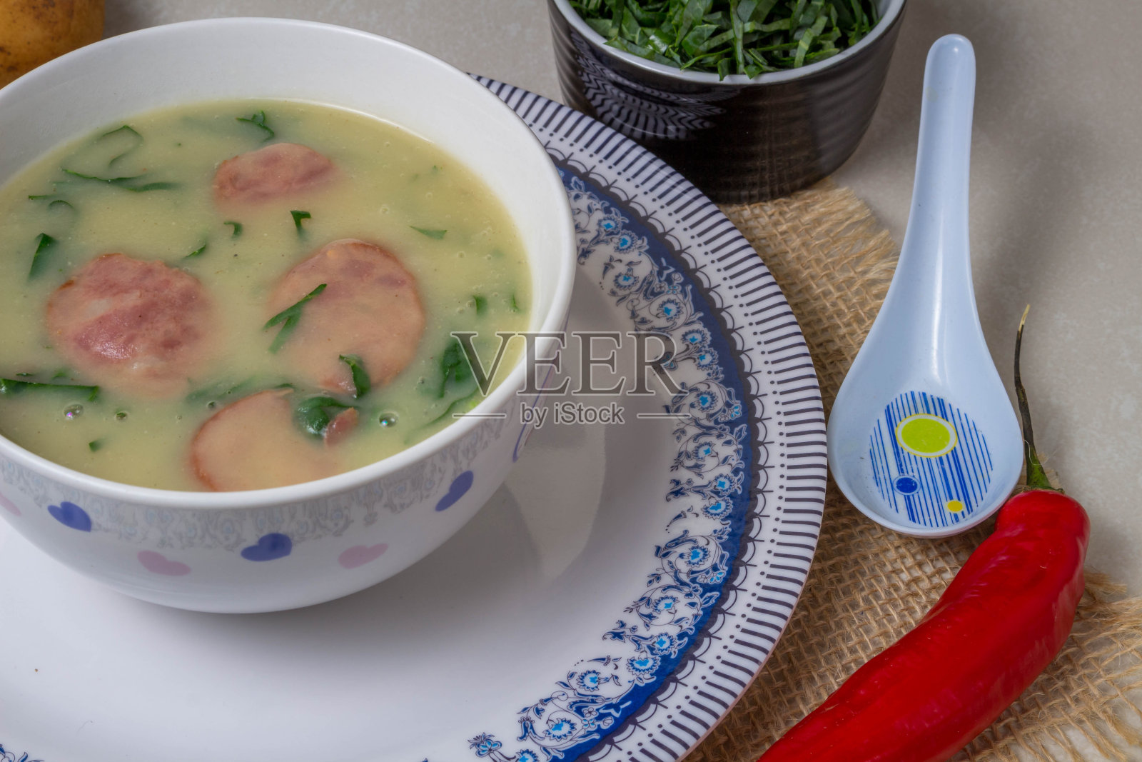 佛得角汤是葡萄牙美食中很受欢迎的一种汤，在陶瓷碗里放上绿色蔬菜和切碎的西班牙辣香肠，再加上一片面包和胡椒。俯视图照片摄影图片