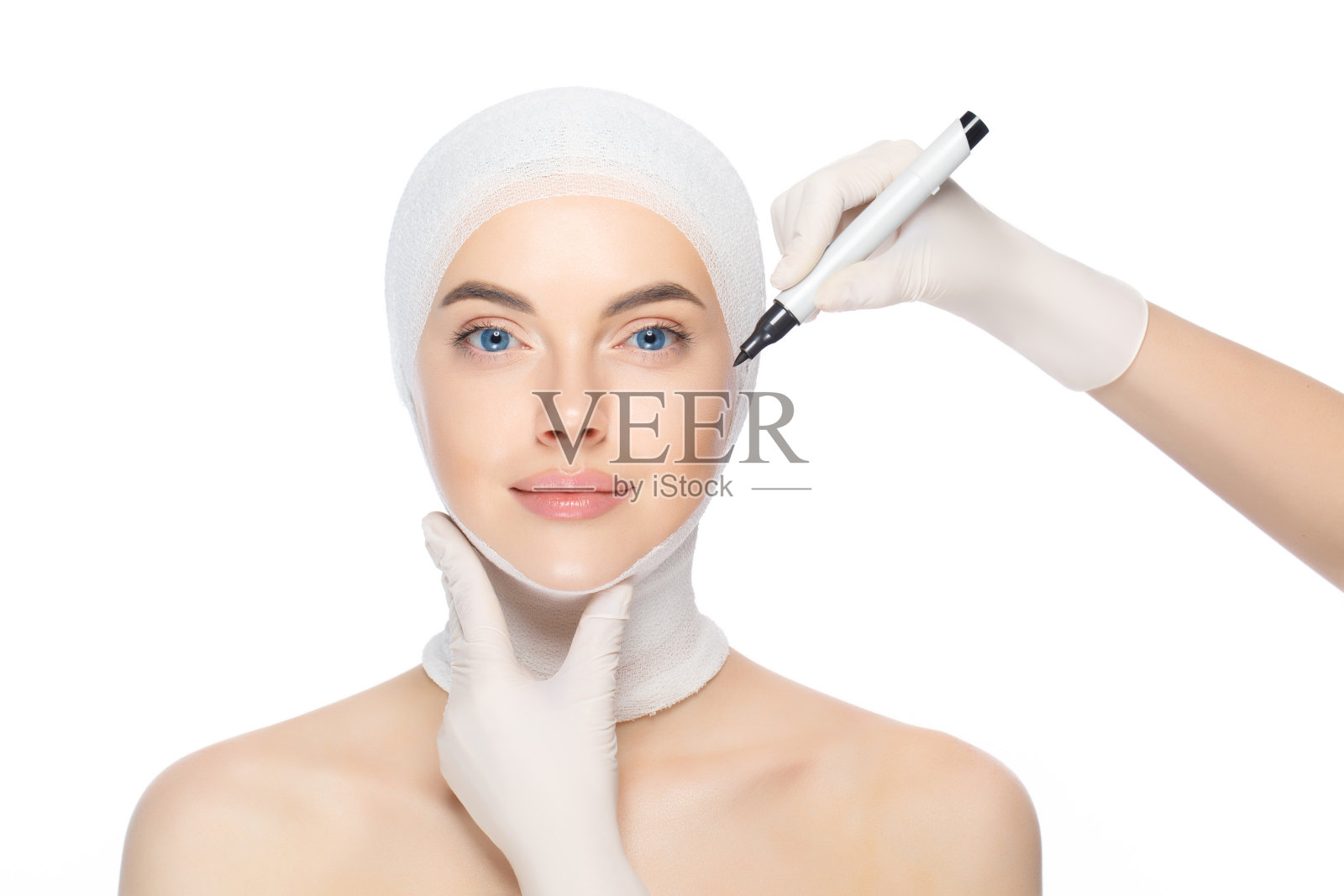 年轻美丽的女性与头部包裹，准备整形手术的医生使用皮肤标记，孤立在白色背景。美实践概念照片摄影图片