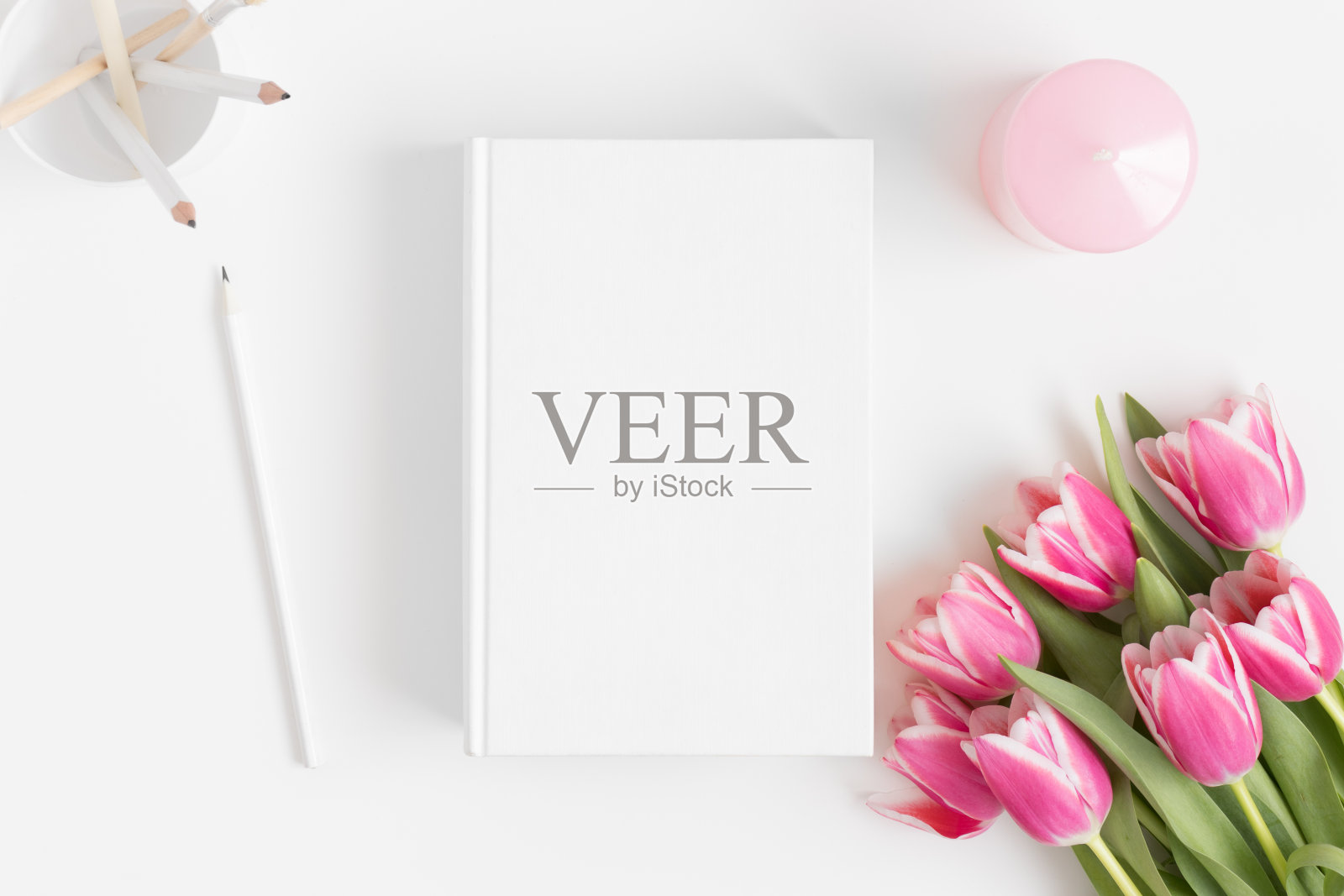 顶视图的一本书模型与一束粉红色郁金香和工作配件在白色的桌子上。照片摄影图片