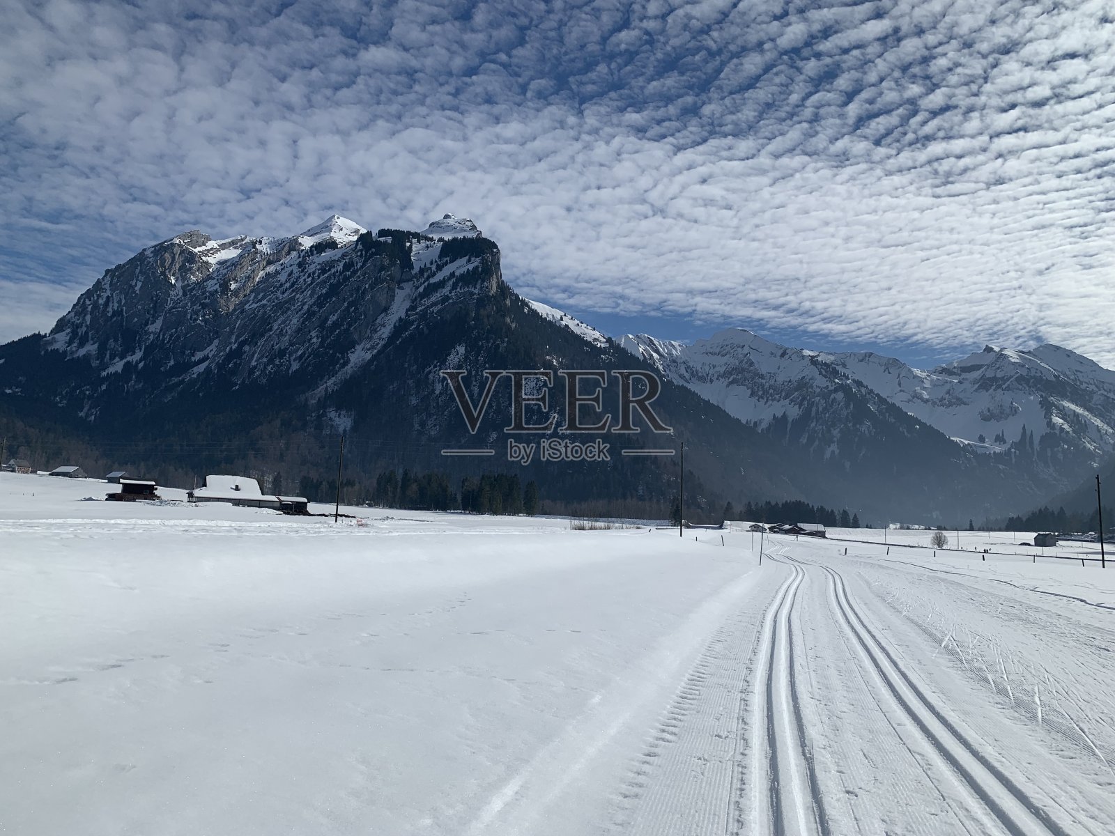 在瑞士施维茨州的学生地区为经典和滑冰风格准备的越野滑雪道。这条小路穿过平坦的地形。背景是阿尔卑斯山脉，天空被卷云略微覆盖。照片摄影图片