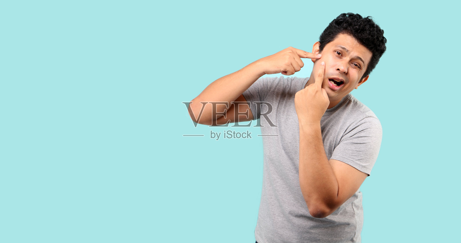 英俊的亚洲男人触摸他的脸。挤痘痘，浅蓝色背景在工作室与复制空间。照片摄影图片