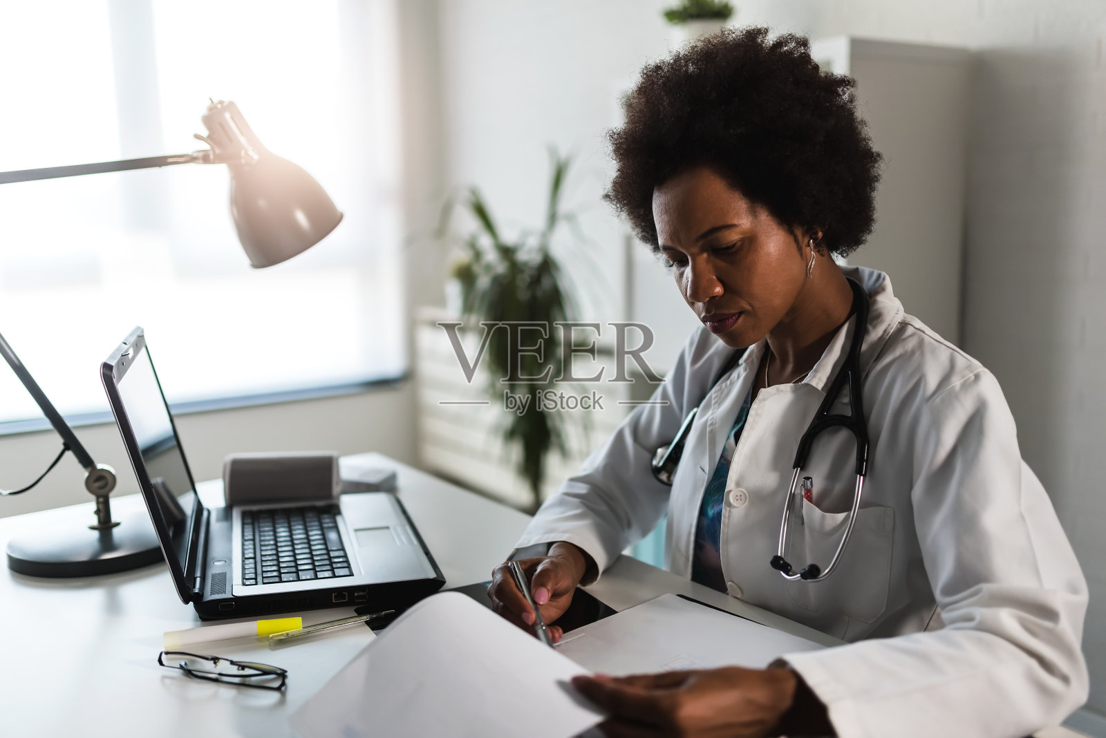 女医生与听诊器看医学文件在她的办公室努力工作照片摄影图片