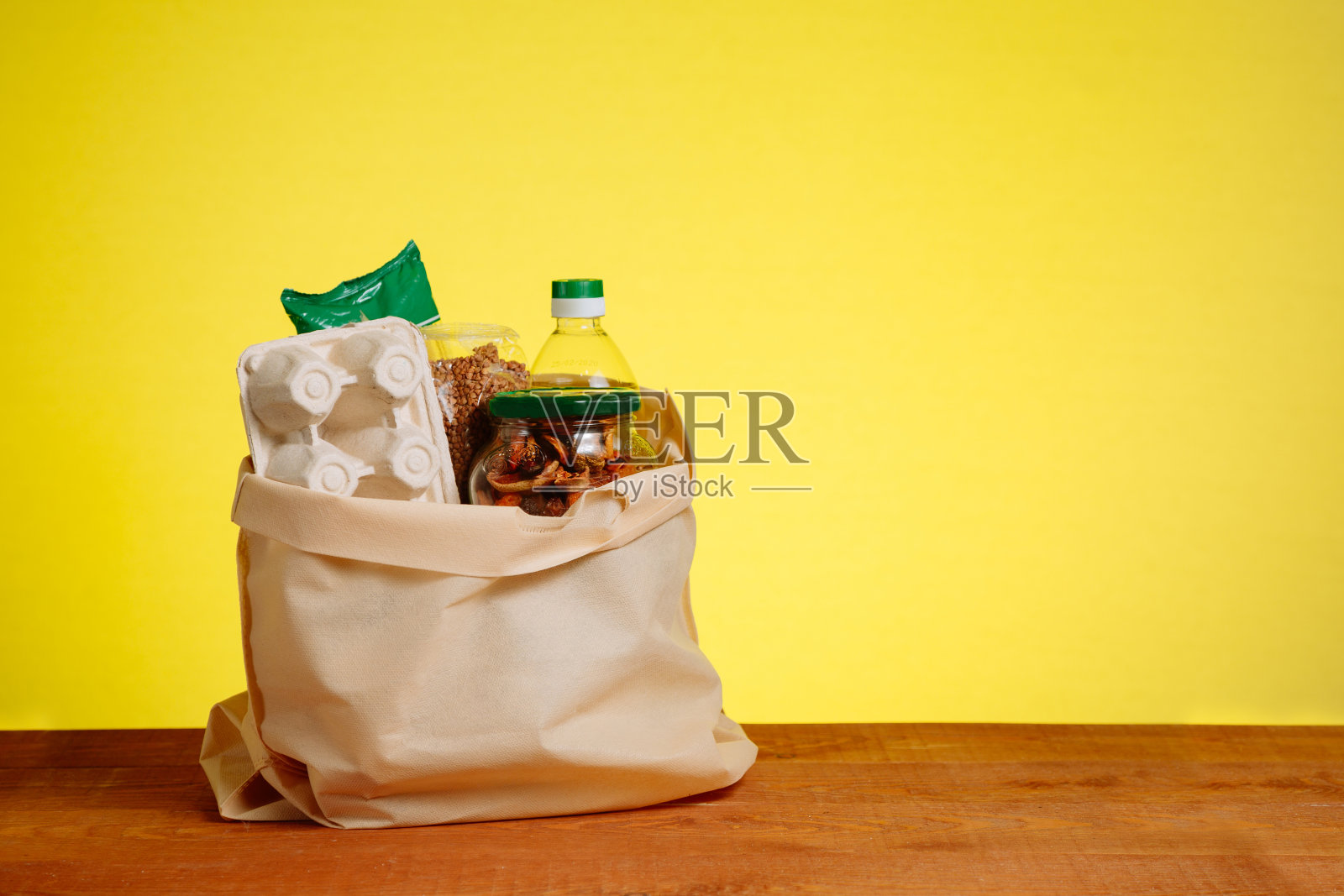 木桌上，黄色背景上，纸袋装着不同的食物。超市购物的概念照片摄影图片