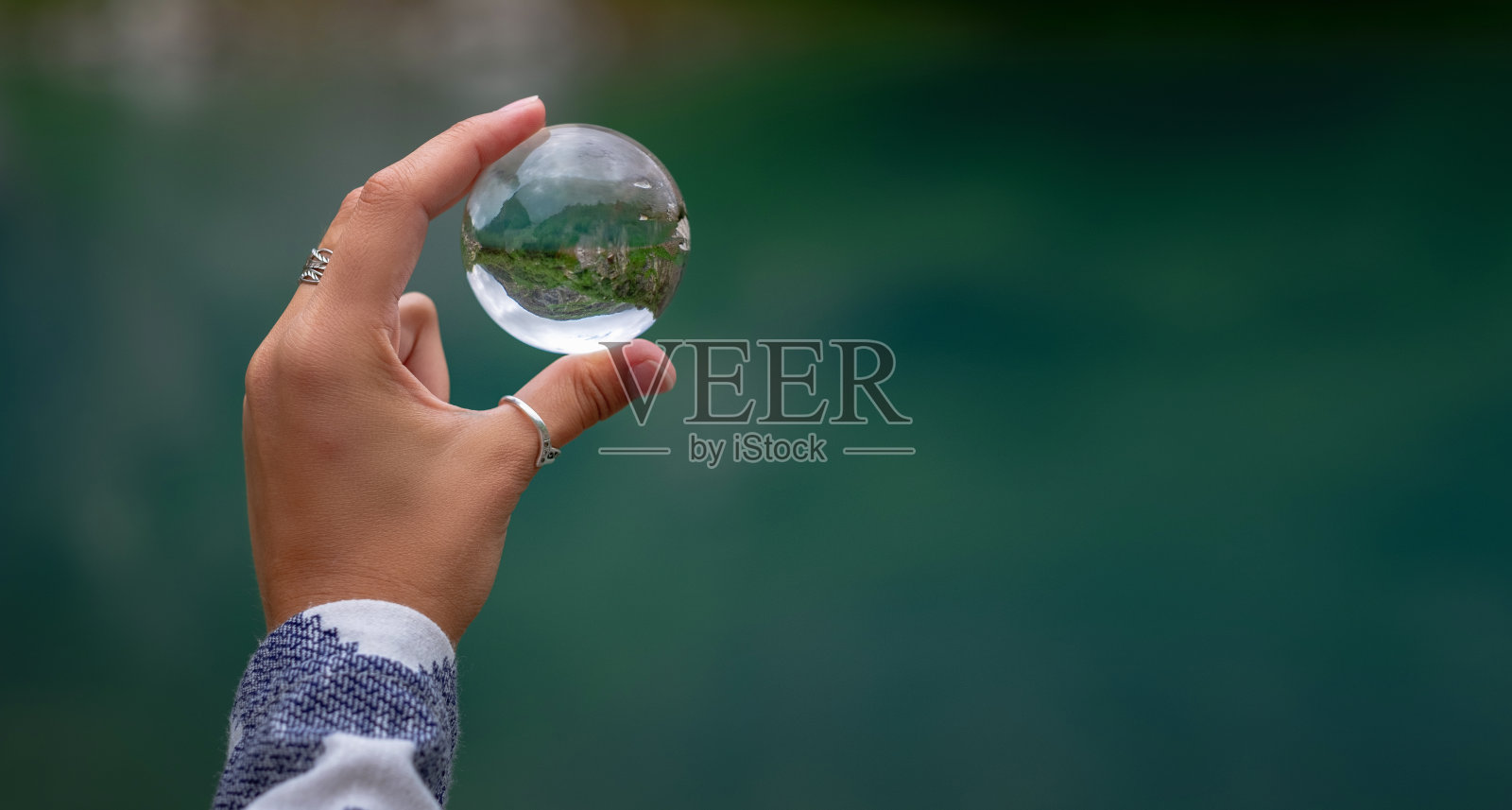 一个女人的手拿着一个球形的玻璃球，背景是一个美丽的山湖。照片摄影图片
