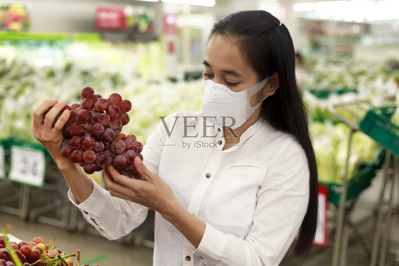 亚洲妇女长头发戴着保护面罩在超市百货公司。女性，在杂货店买水果。新冠肺炎疫情后的新常态。家庭的概念。软焦点的照片。照片摄影图片