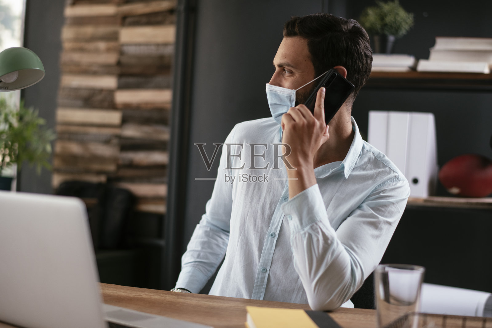 戴着医用口罩的年轻商人在打电话。照片摄影图片