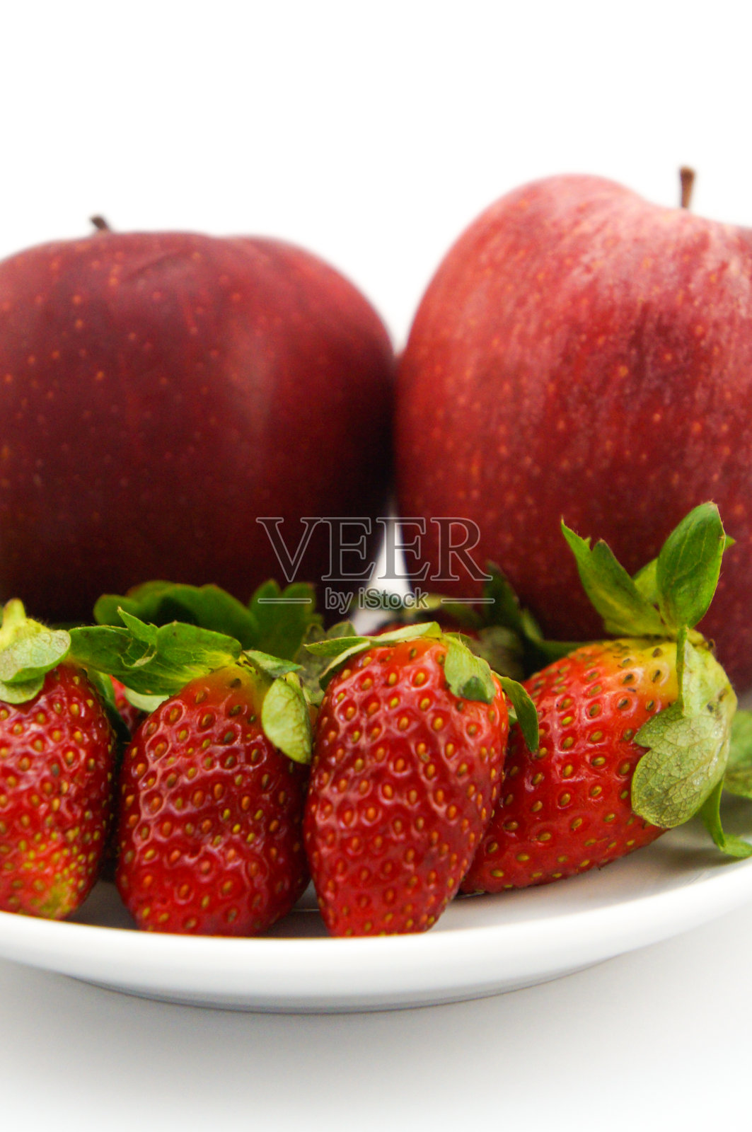 红色的水果在盘子里。苹果和草莓。白色背景照片摄影图片