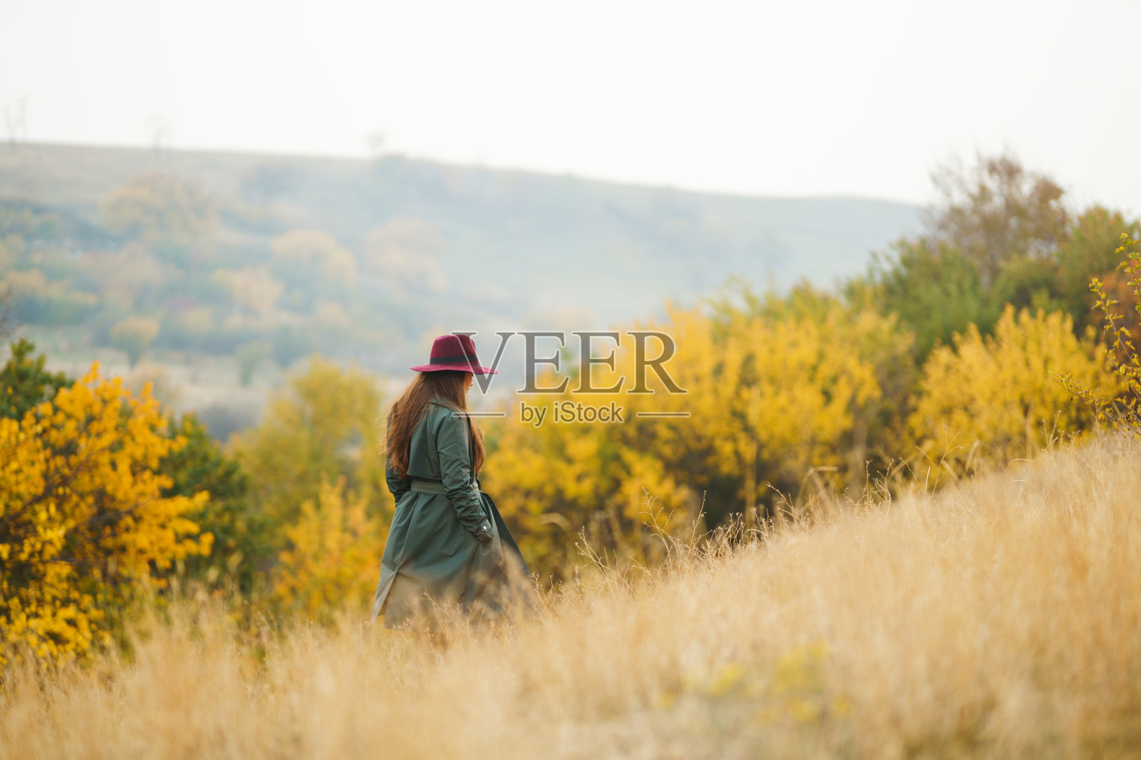 穿着大衣戴着帽子的优雅女子漫步在秋天的公园里。照片摄影图片