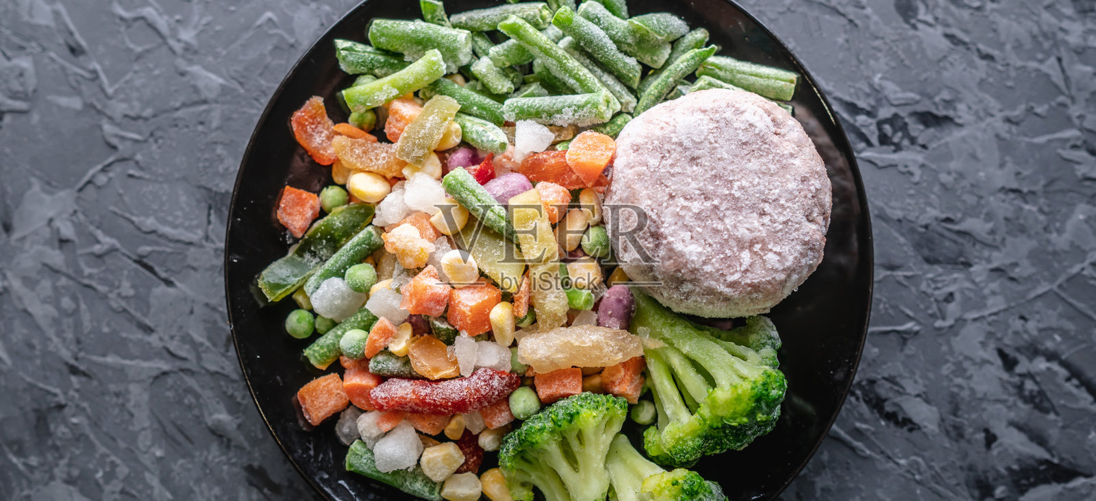 灰色的桌子上放着一盘冷冻蔬菜和一份肉排。节约做饭时间和方便储存速冻菜肴的理念照片摄影图片