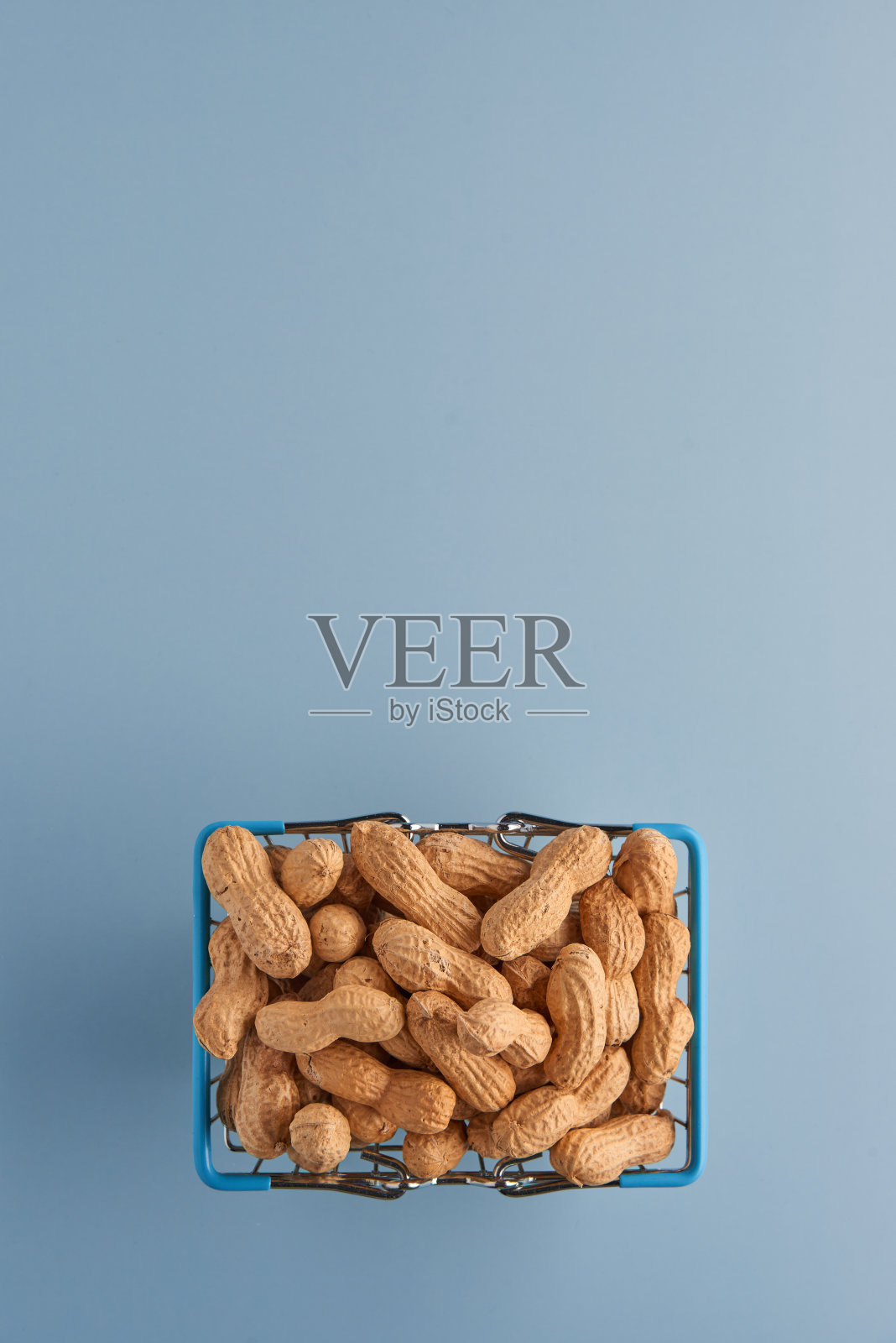 烤未剥皮花生在购物篮孤立在蓝色背景。食品、配料、有机素食蛋白、健康饮食营养理念。顶部视图与复制空间。照片摄影图片