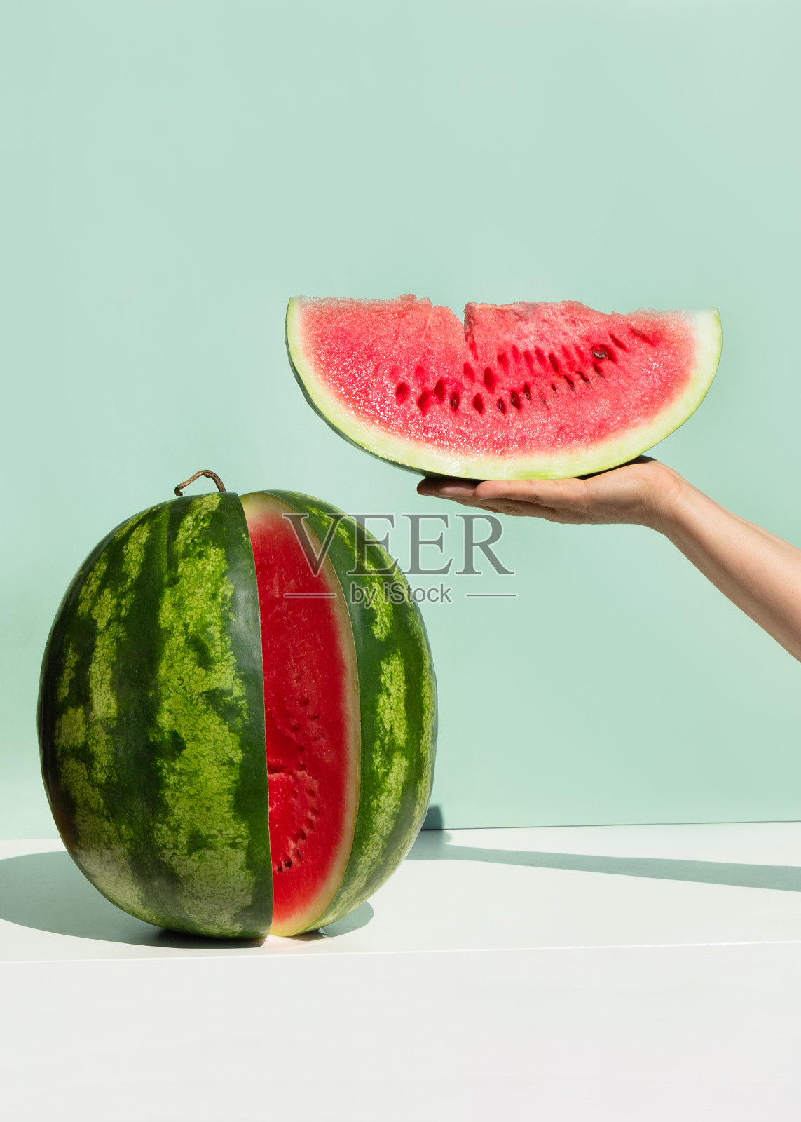新鲜成熟的西瓜，新薄荷色背景。女人的手拿着一片西瓜。极具创意的夏季水果概念。照片摄影图片
