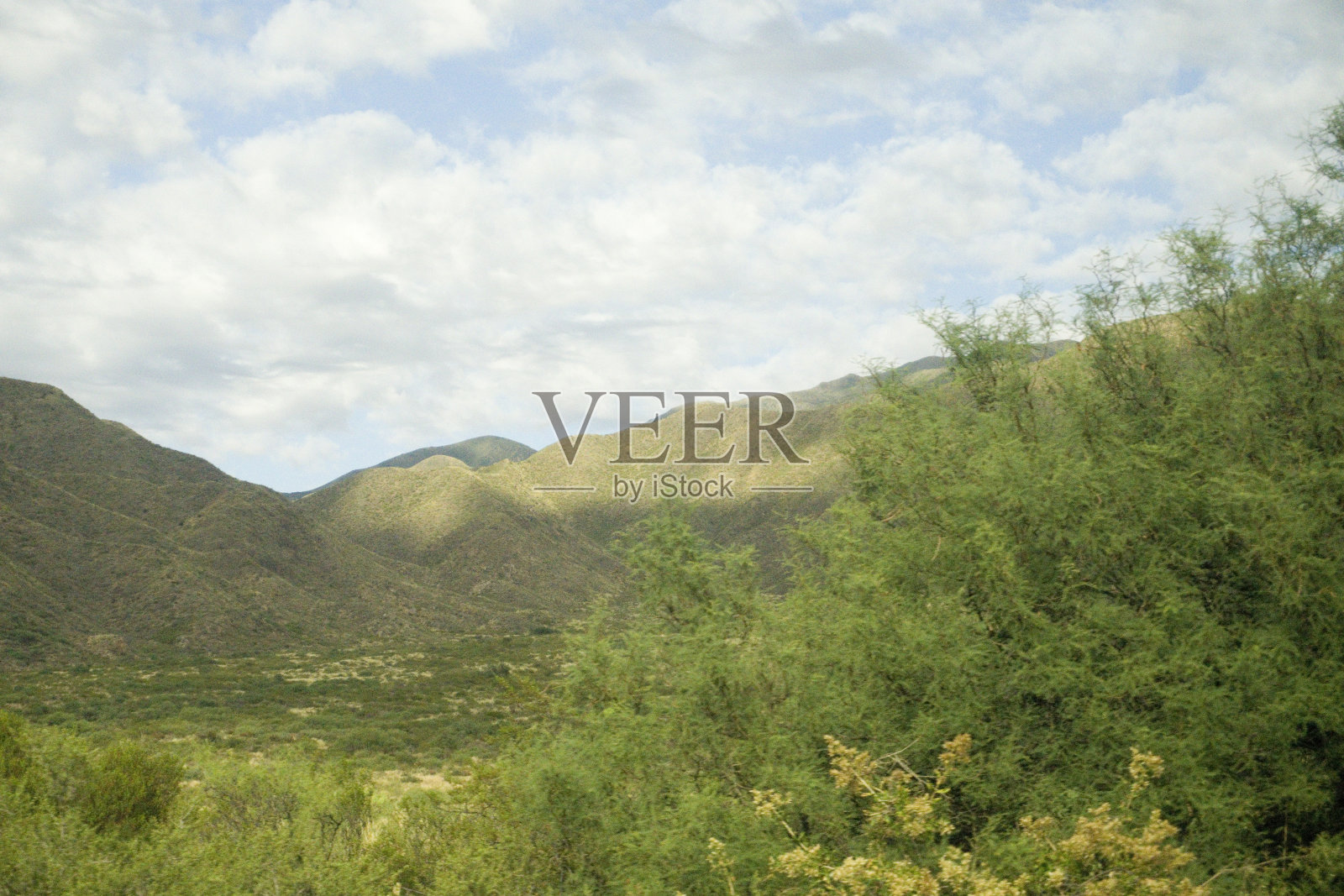 景观岩石山脉在不同的阴影与植被，灌木的土地前面与多云的天空门多萨，阿根廷照片摄影图片