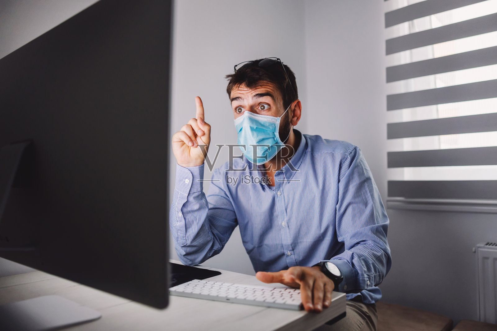 年轻有魅力的员工戴着口罩坐在他的办公室里，并有办法解决冠状病毒爆发期间的问题。照片摄影图片