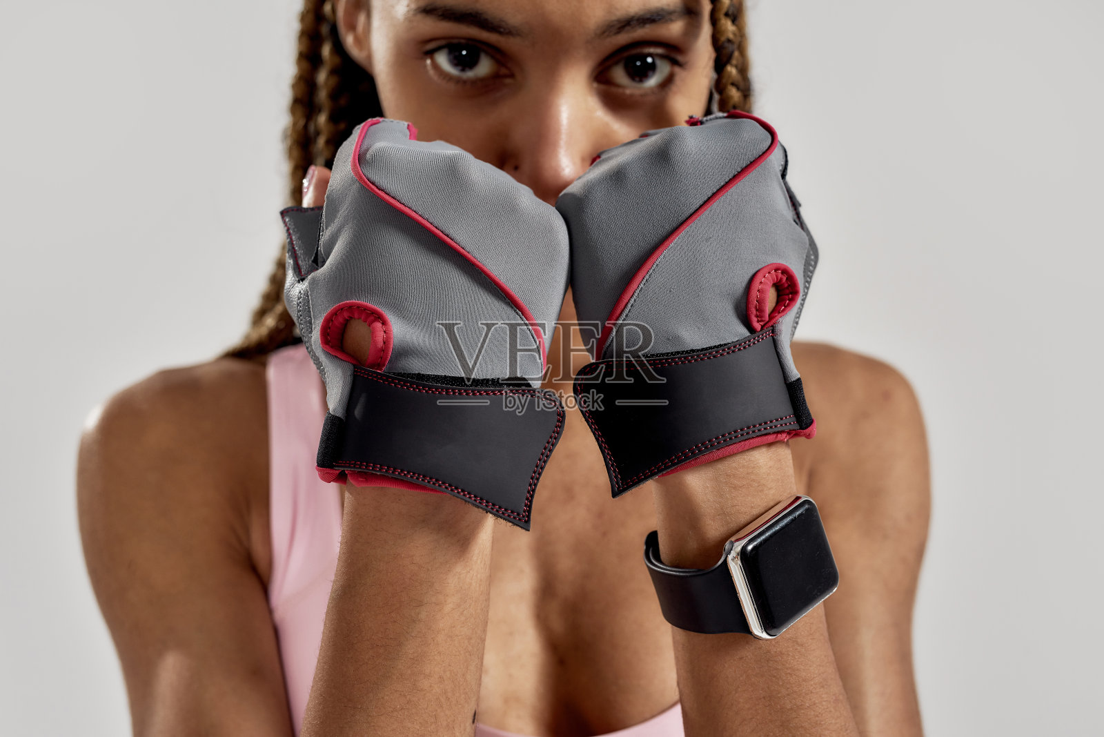 裁剪的肖像年轻的运动混合种族妇女在运动服看相机，戴着健身手套，而摆出孤立的灰色背景。健康的生活方式和运动理念照片摄影图片