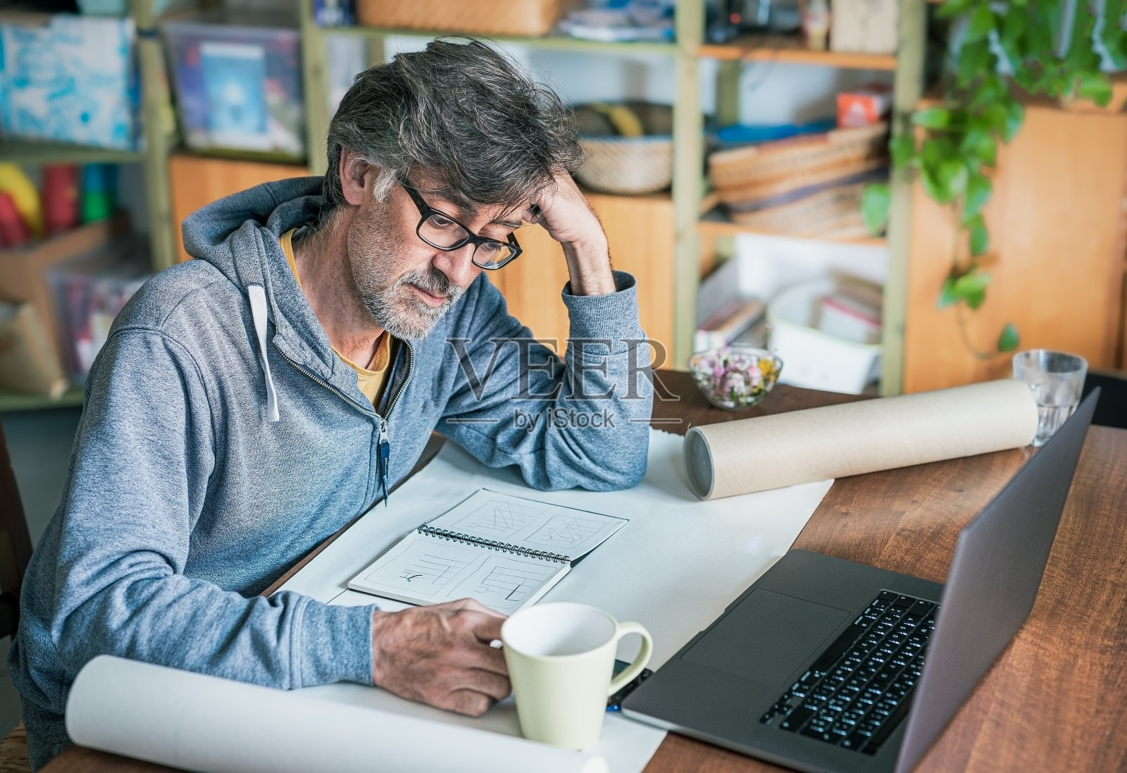 有创造力的人，头发和胡子花白，在家里为一些项目工作，在一个白色的笔记本上绘制想法，连接他的笔记本电脑，专注于男人，聪明的工作理念的设计师或建筑师照片摄影图片