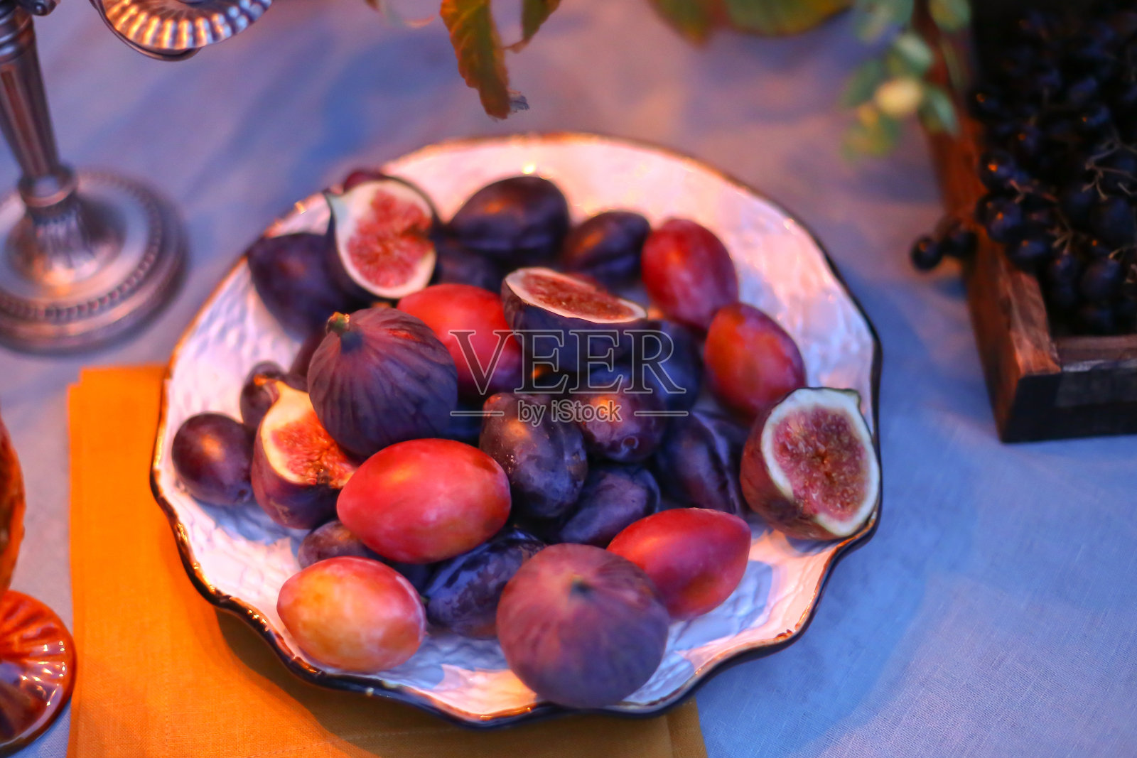 盘子里放着成熟的大无花果。秋夜户外浪漫晚餐。餐桌上有桌布和装饰白色的盘子，酒杯，餐巾，餐桌设置烛台。食品造型的概念照片摄影图片