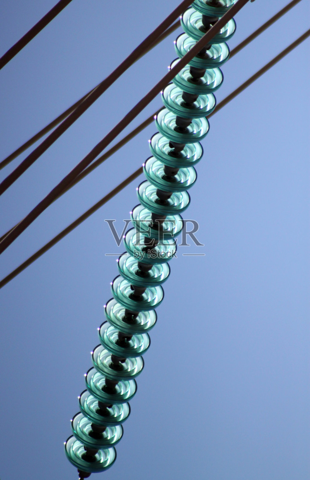 在明亮的蓝色天空下，绿色的绝缘体和电线的抽象镜头照片摄影图片