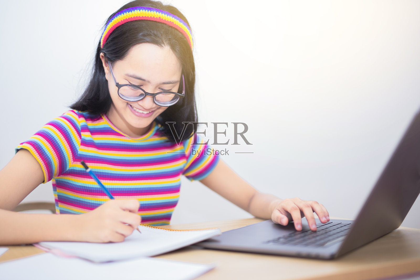 远程学习在线教育，微笑的女孩学生在线学习skype老师，快乐的年轻女子学习语言听结构看网络研讨会写笔记看笔记本电脑。照片摄影图片