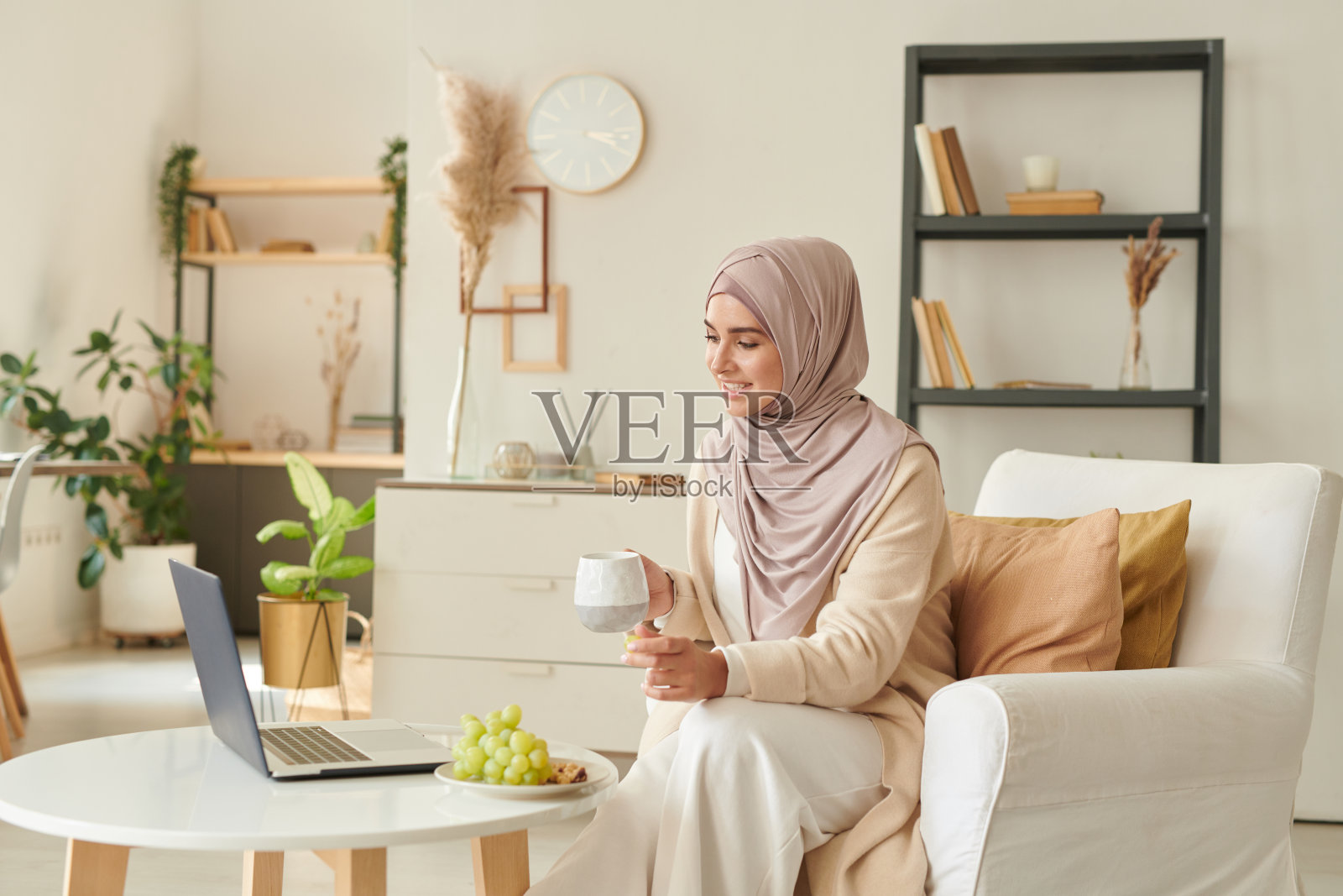 现代穆斯林妇女在家喝茶和看喜剧电影的空闲时间在笔记本电脑上照片摄影图片