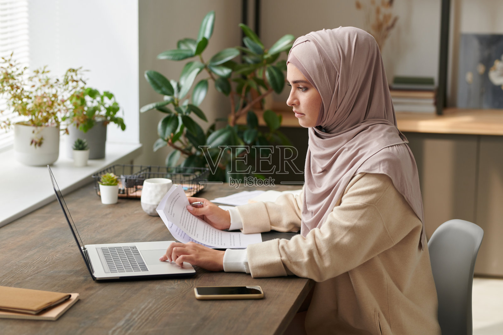 严肃的年轻女子戴着头巾坐在办公桌前，在现代的办公室里独自从事新的商业项目照片摄影图片