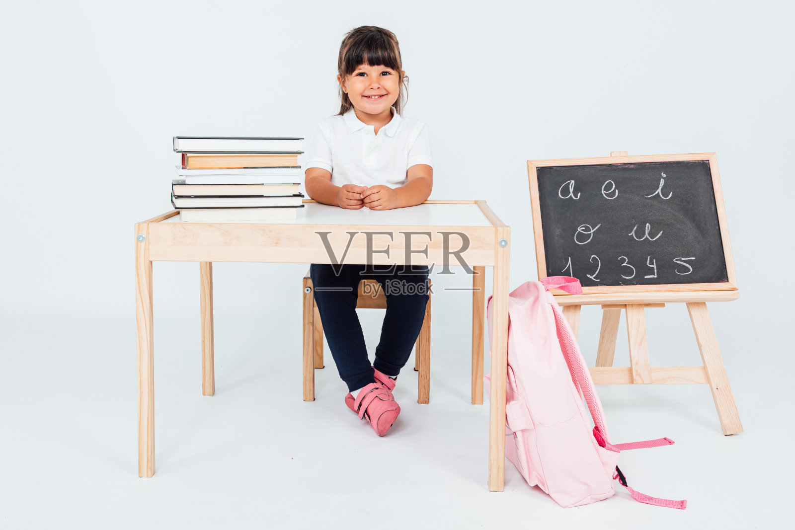 小女孩在学校，微笑着坐在椅子旁边的白色背景的书。学校的概念照片摄影图片