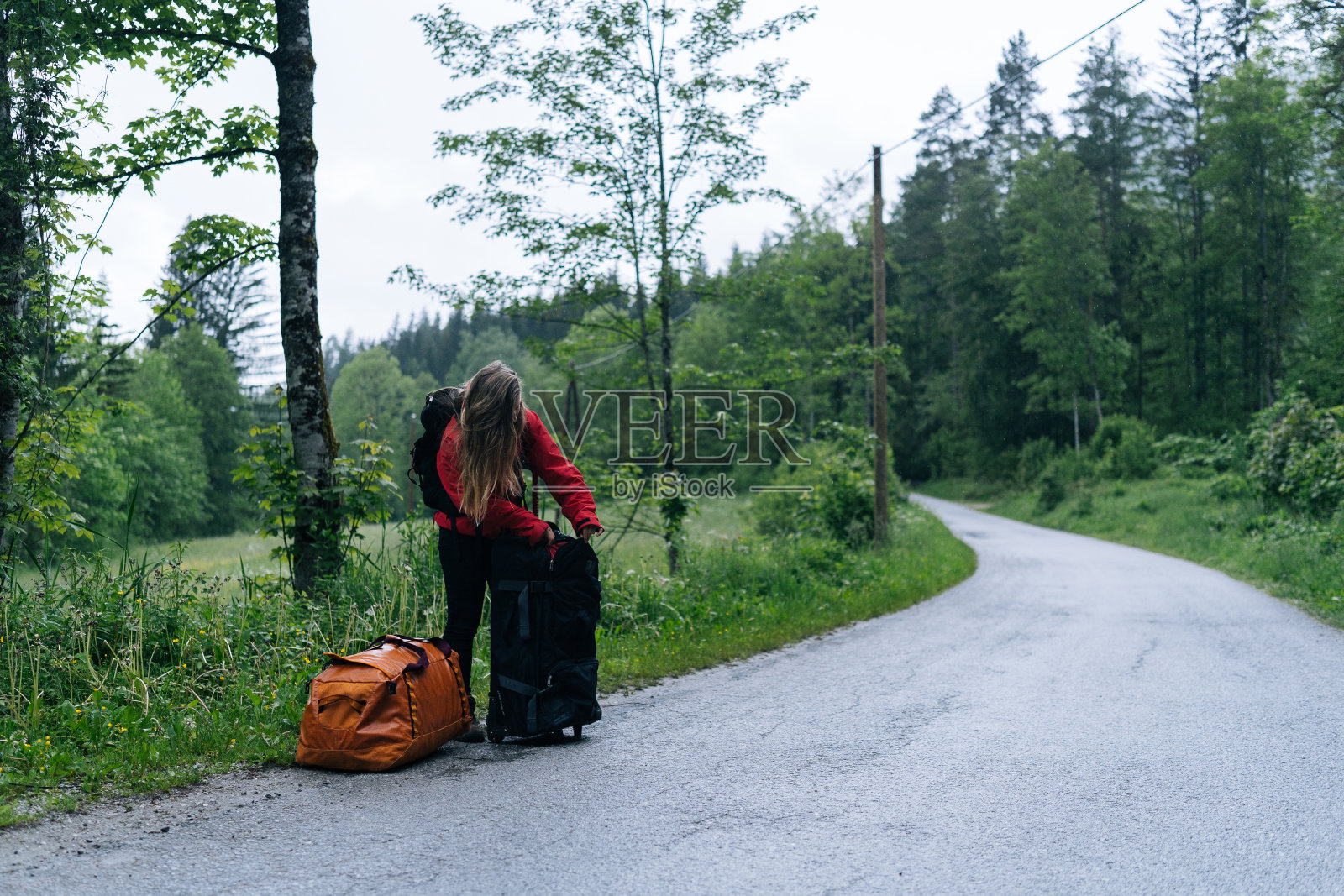 年轻女子背包客在雨中等待在路边与行李照片摄影图片