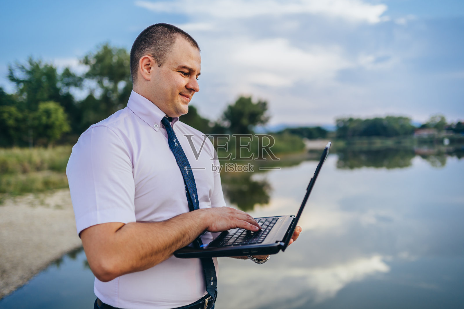 商人站在湖边使用笔记本电脑照片摄影图片