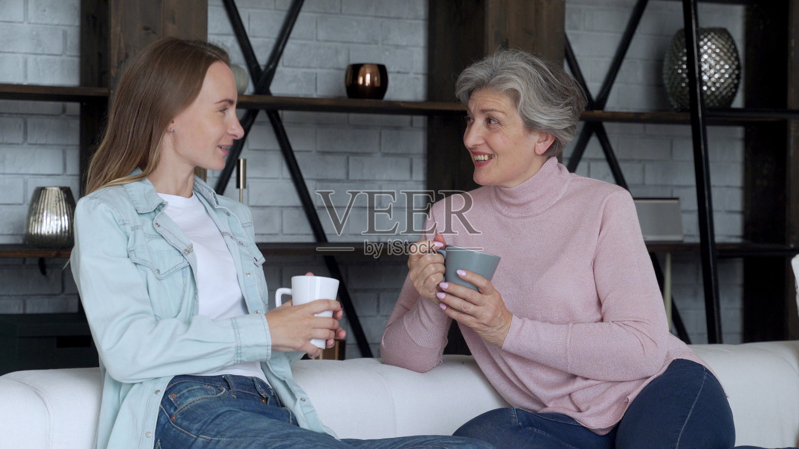 成熟的母亲和她成年的女儿坐在家里的沙发上，一边喝着咖啡，一边谈笑照片摄影图片